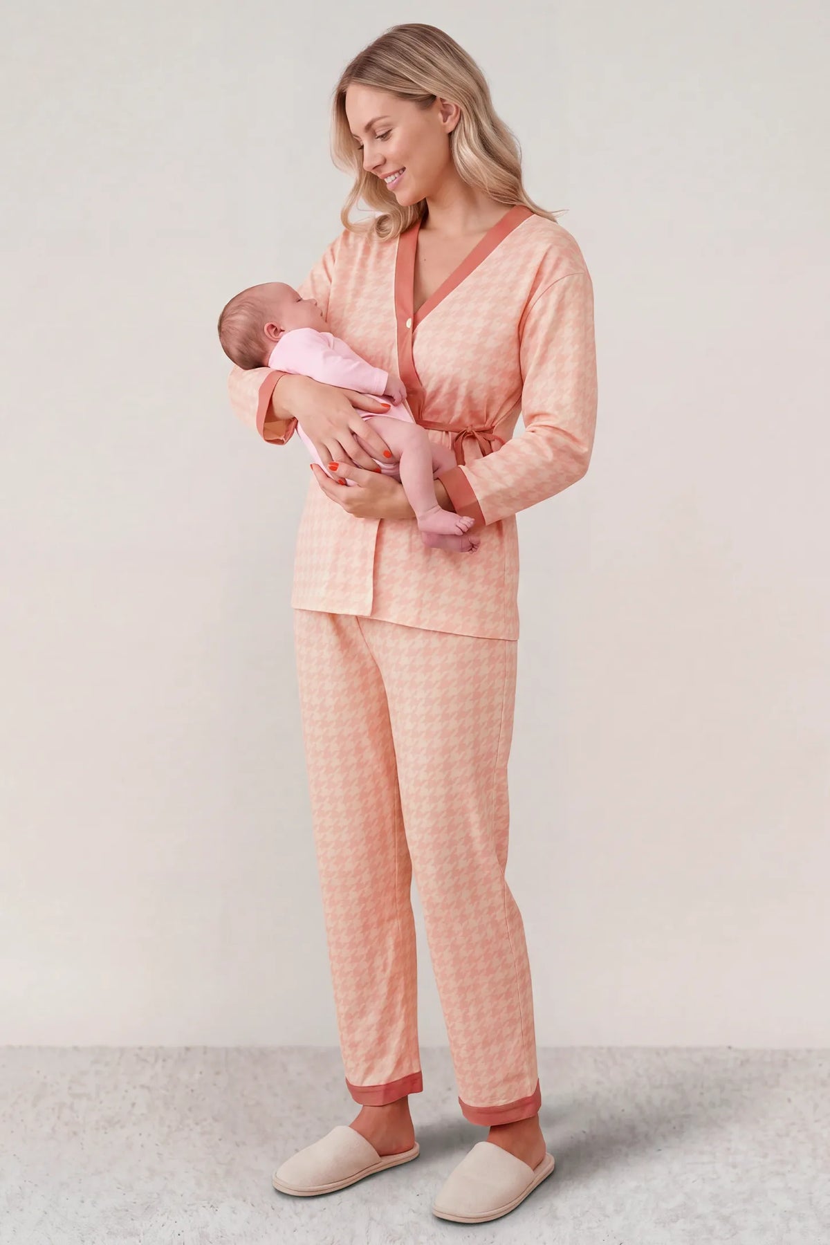 Cotton Houndstooth Nursing Pajama Set in Pink Houndstooth featuring postpartum nursing functionality, soft cotton comfort, and wrap tie waist on a mother holding her newborn baby, standing front view.