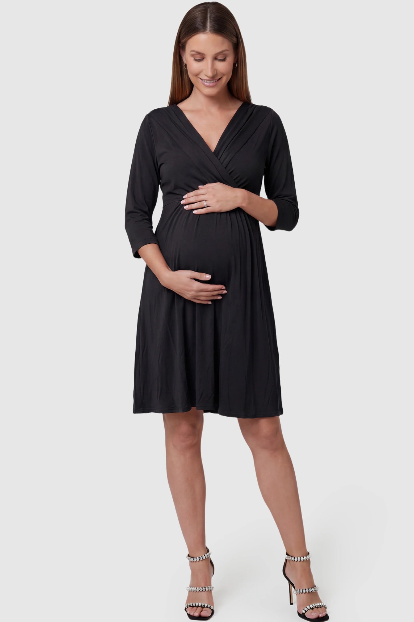 Crossover A-line maternity & nursing midi dress in black with wrap-style V-neck bodice, front view on pregnant model