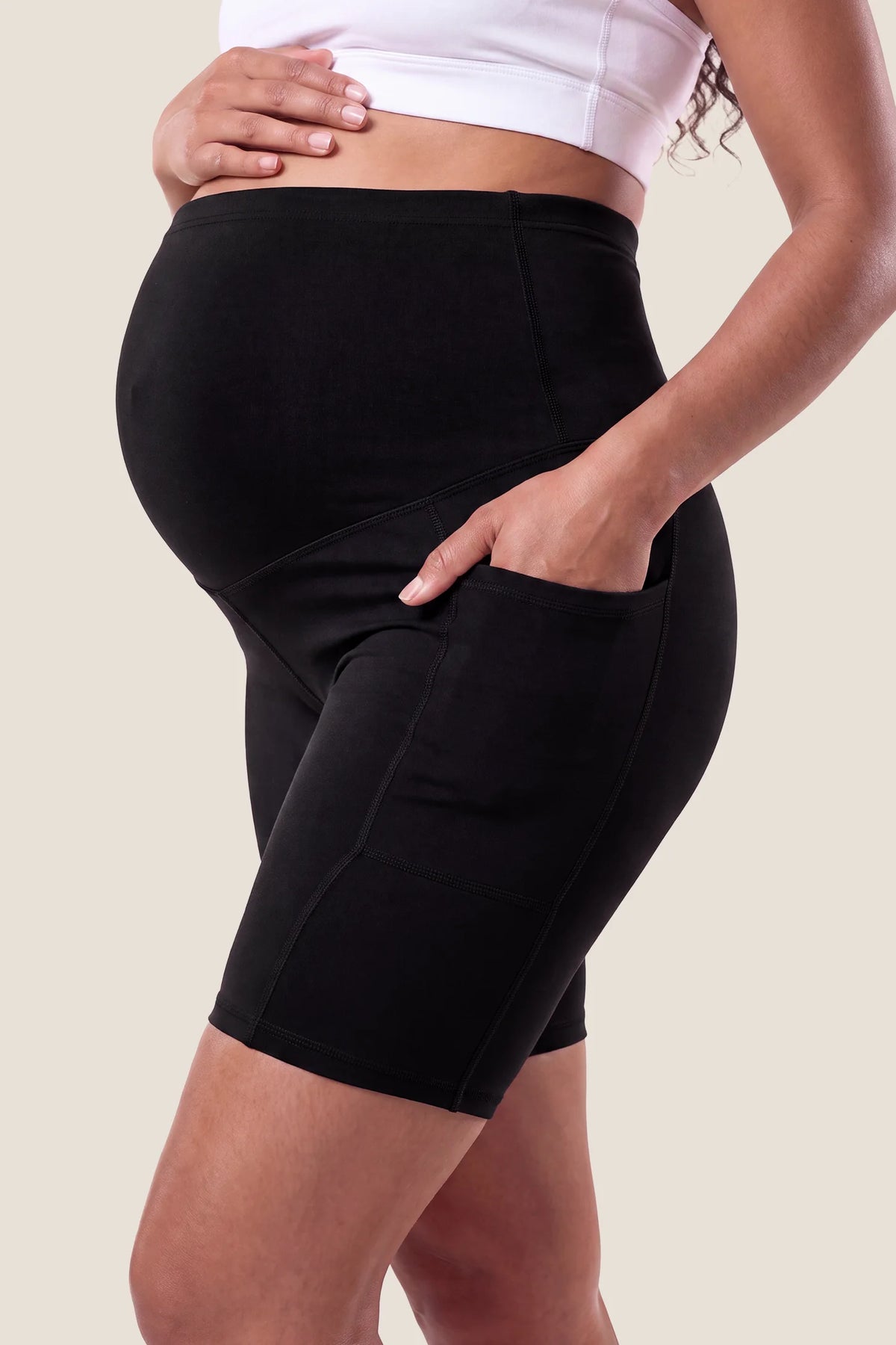 High-rise stretch biker maternity shorts in black featuring seamless fit, mid-thigh length, and supportive belly panel on pregnant model. side view