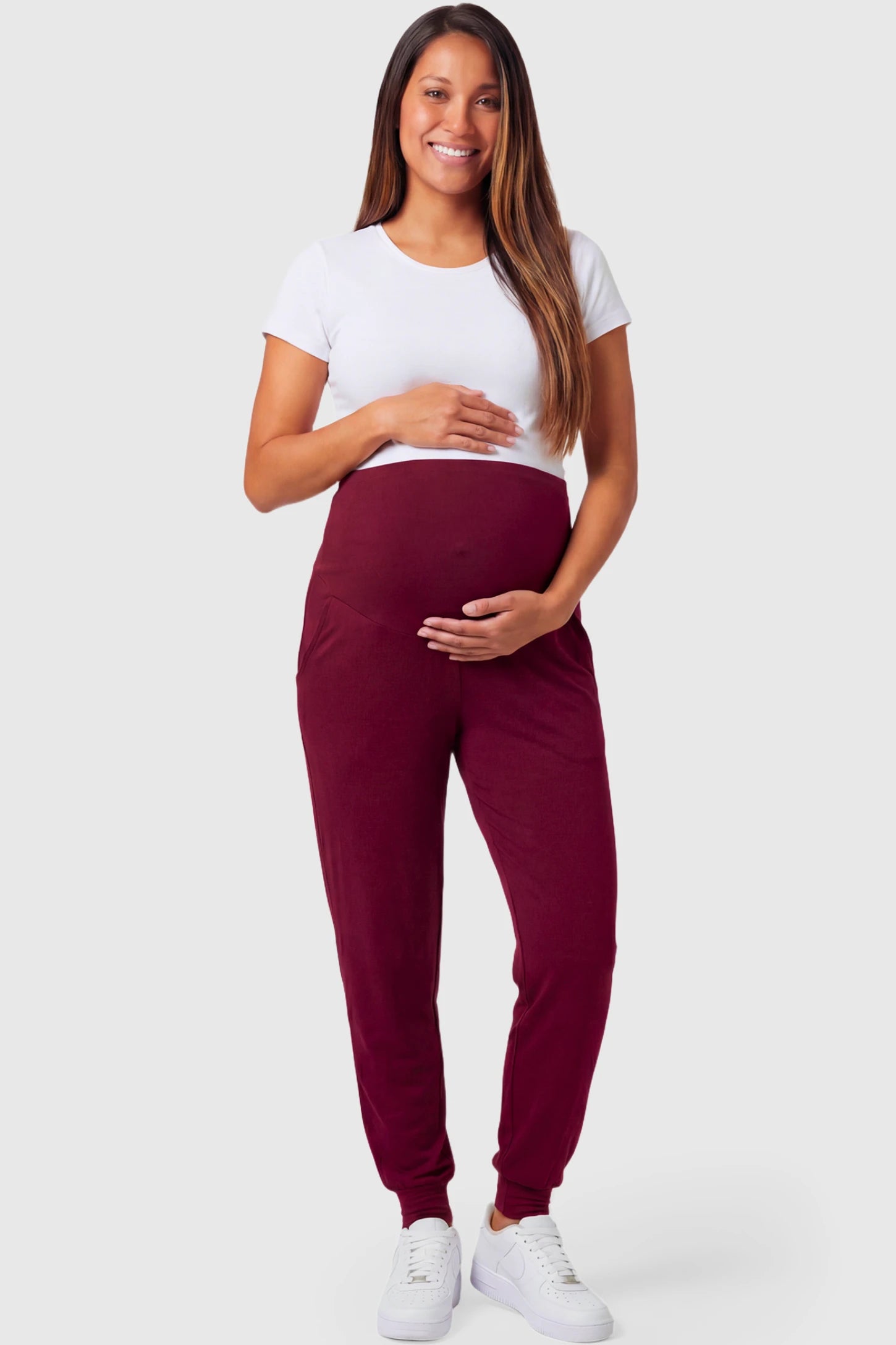 Full-Panel Cuffed Maternity Joggers in wine red featuring high-rise over-the-belly panel, ribbed cuff hem, and side pockets on pregnant model.