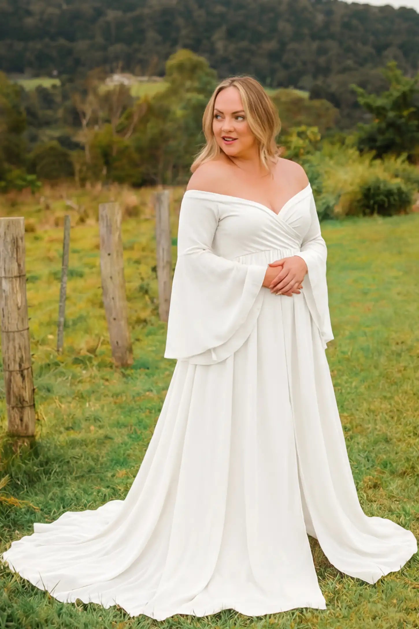 Off-the-shoulder long train maxi maternity dress in white featuring off-shoulder and long-train in full body front view on a editorial lifestyle model