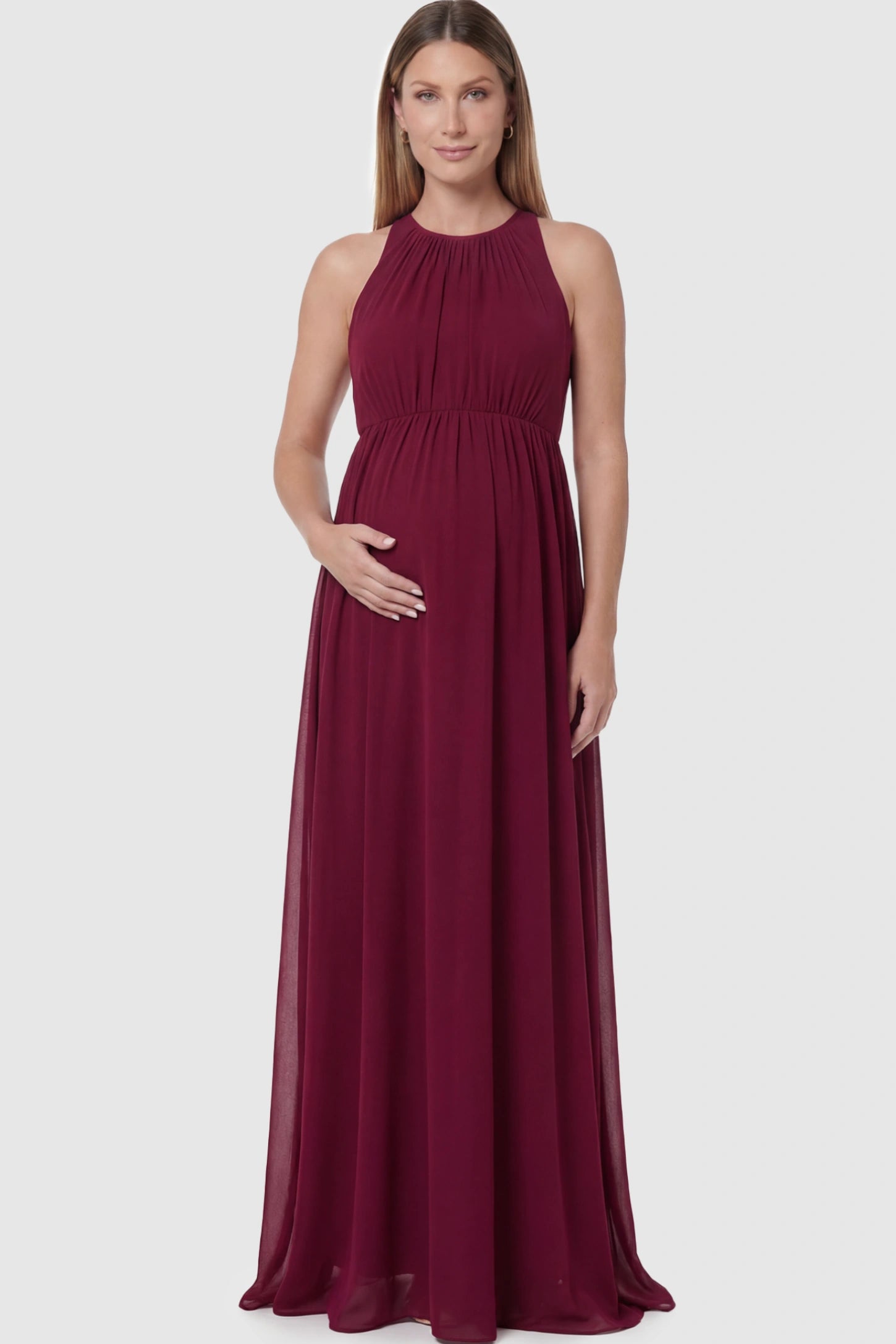Pleated Mesh Sleeveless Maternity Maxi Dress in burgundy with an empire waist on a pregnant model.