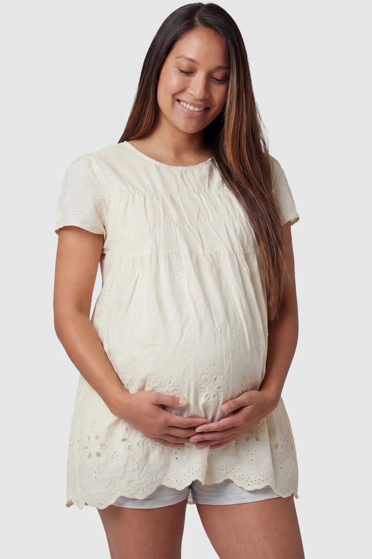 Floral eyelet round neck peplum maternity top in pale yellow with delicate floral eyelet detail, front view on pregnant model