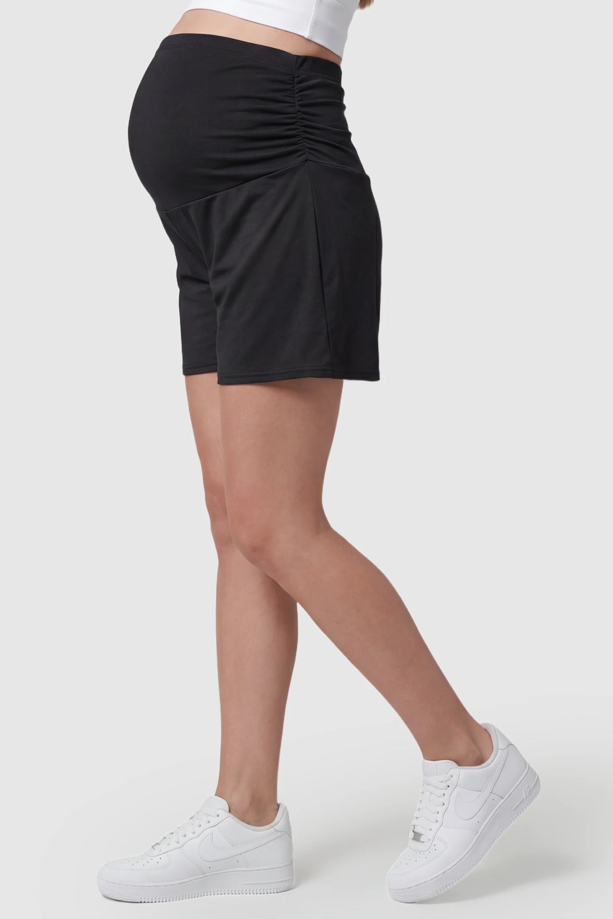 Full Panel Relaxed-Fit Maternity Shorts in black featuring seamless belly band and mid-thigh length on pregnant model side view.