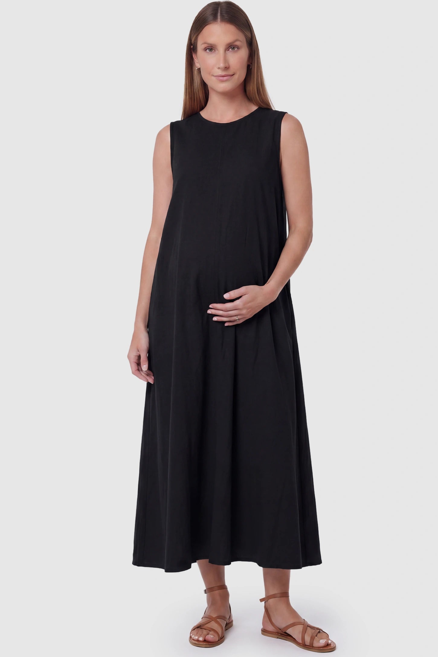 Sleeveless pocketed longline hem maternity midi dress in black with sleeveless design and longline hem, front view on pregnant model
