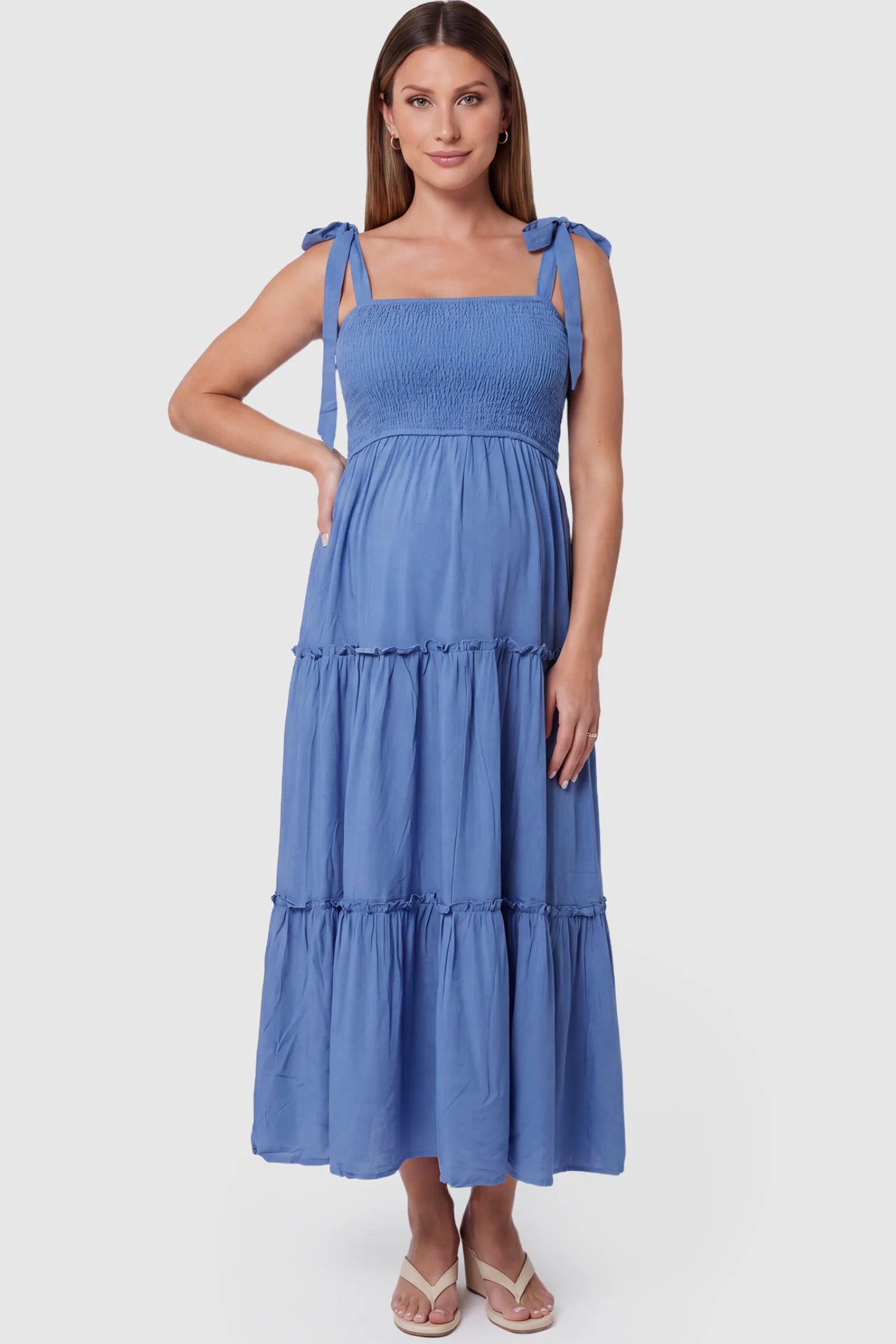 Smocked square neck tiered maternity midi dress in blue with square neckline, smocked bodice, and adjustable tie straps, front view on pregnant model