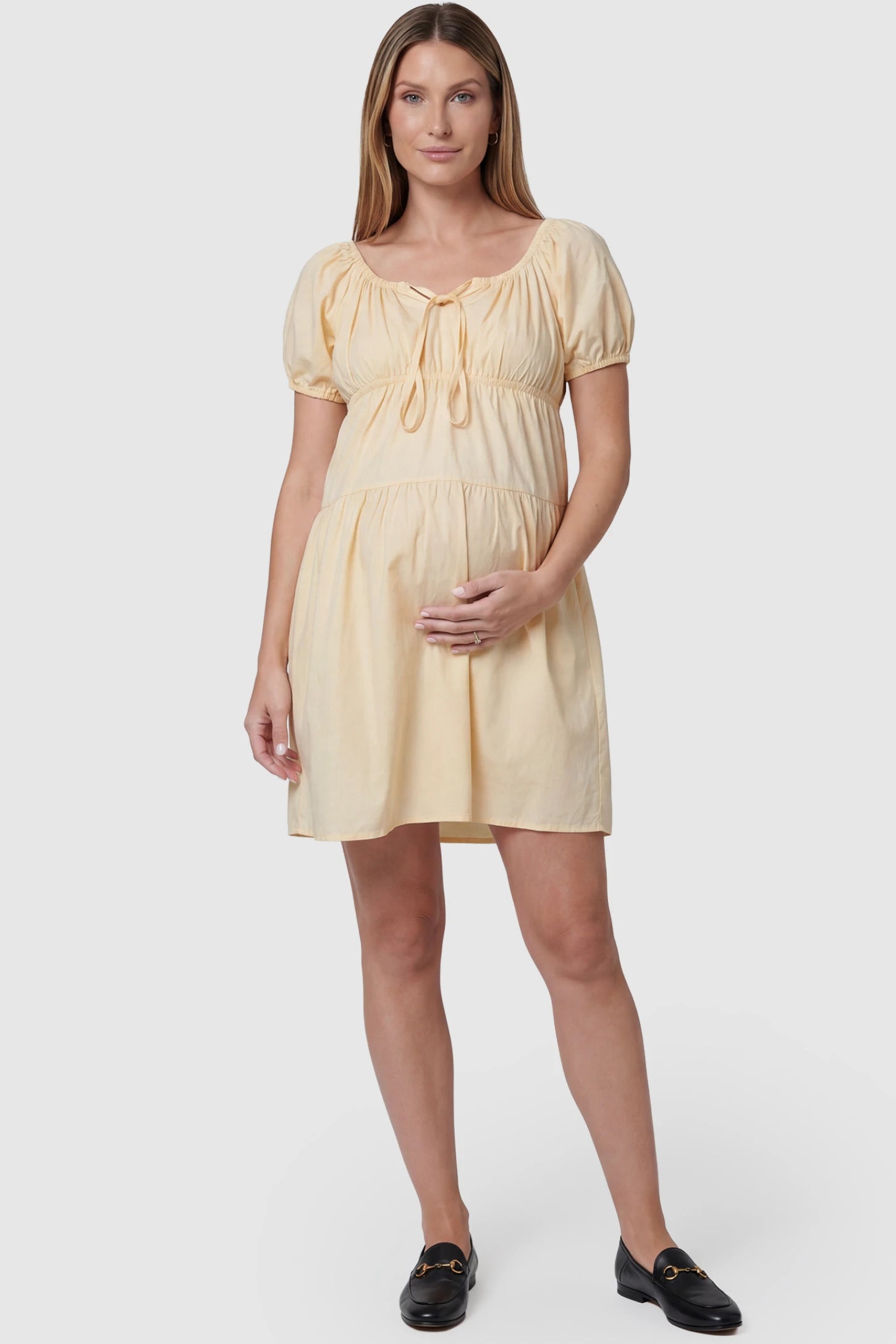 Short sleeve tiered A-line maternity short dress in yellow with bump-flattering A-line fit, front view on pregnant model