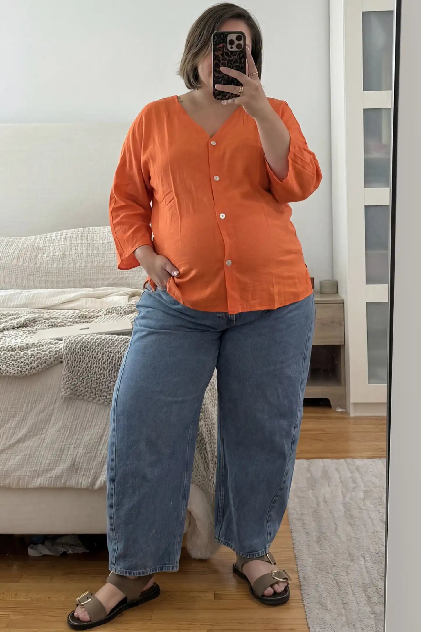Button Down V-Neck Long Sleeve Maternity Top in Orange featuring a relaxed drape on a pregnant woman taking a mirror selfie indoors, front view.