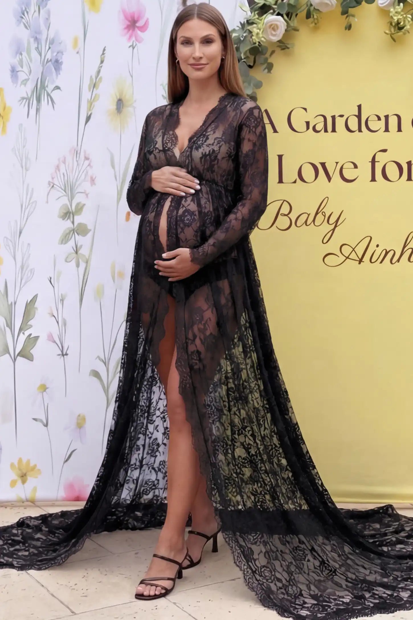 Floral Lace V-Neck Long Sleeve Maternity Photoshoot Gown in Black featuring long sleeves and high front slit on a pregnant model posing front.