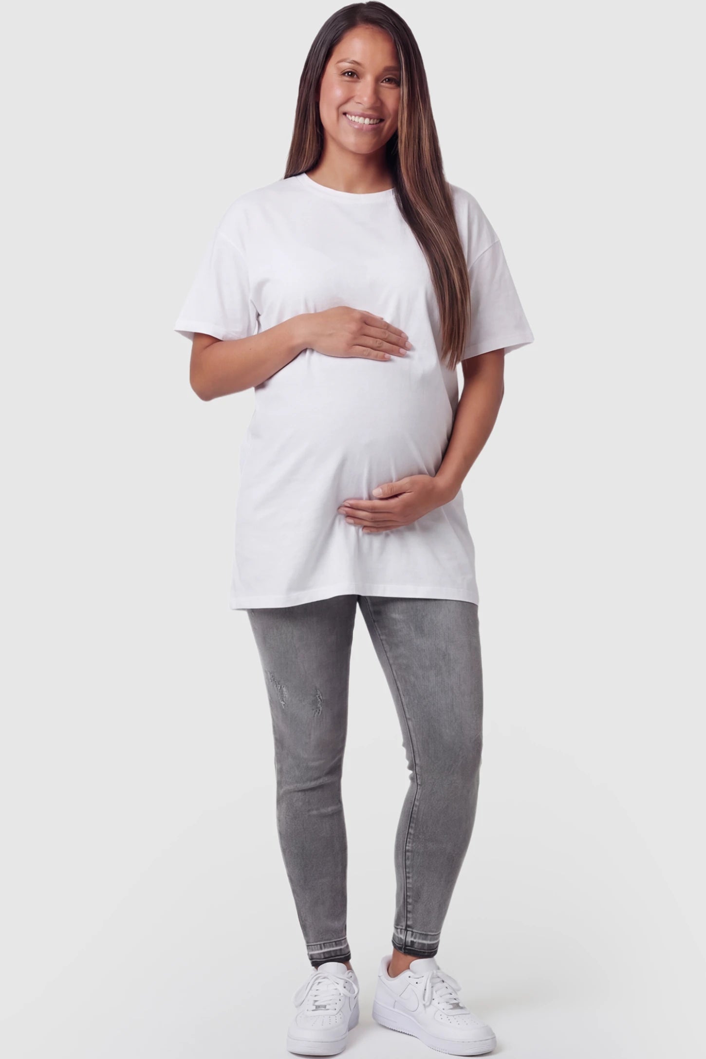 Full Panel Released Hem Maternity Skinny Jeans in Gray featuring a released hem and over-the-belly panel on a pregnant model facing front.