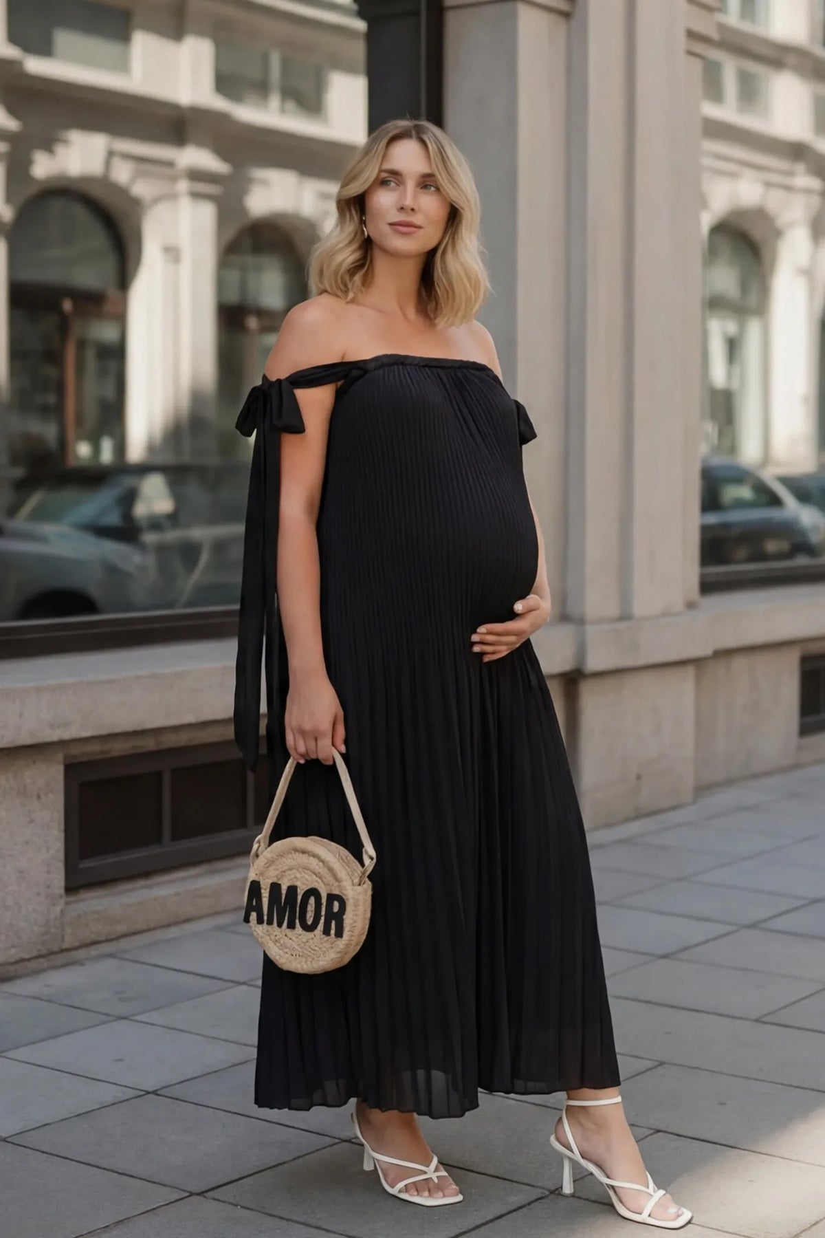 Pleated Braided Cold-Shoulder Maxi Maternity Gown in Black featuring soft pleated fabric on a pregnant model in an editorial lifestyle setting.