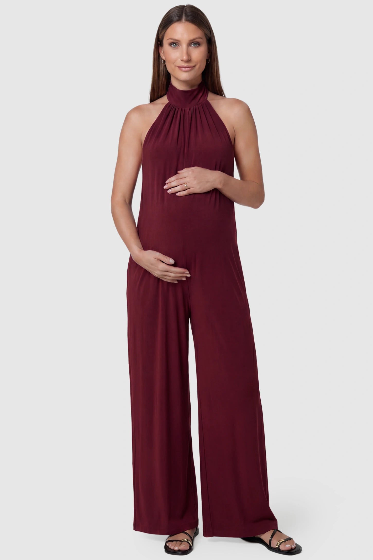 Pocketed Mock Neck Sleeveless Maternity Jumpsuit in rose red featuring a high gathered neckline, side pockets shown on a pregnant model, front view.