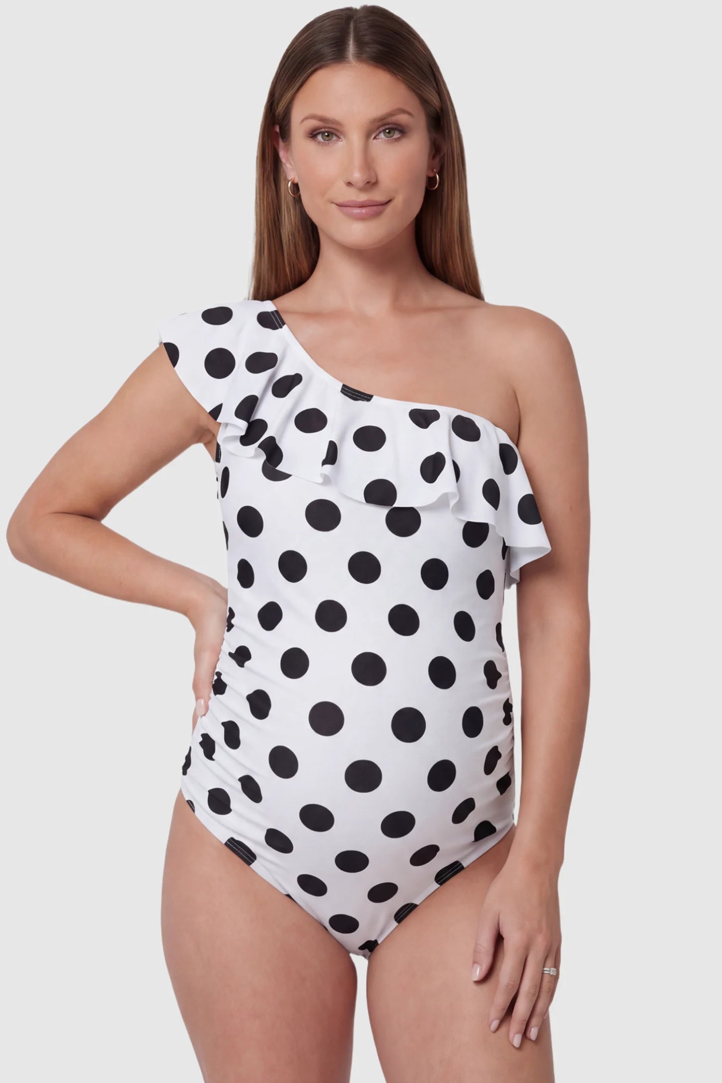 Polka Dot Side Ruched One-Shoulder Maternity Swimsuit in White featuring side ruched panels and ruffle detail on a pregnant model, front view.