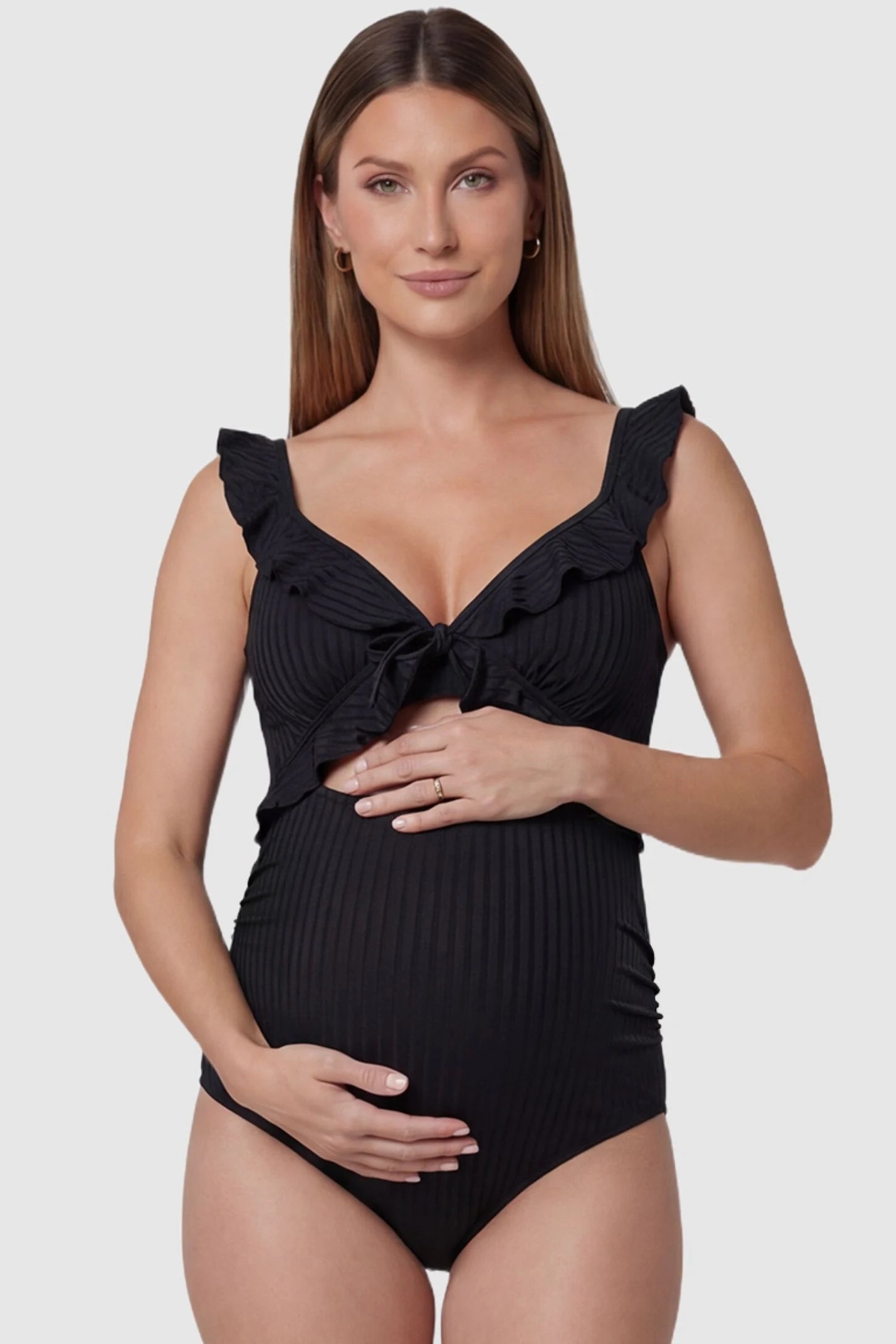 Ribbed Lace-Up Back Maternity One-Piece in Black featuring a ruffled neckline and front cutout on a pregnant model, front view.