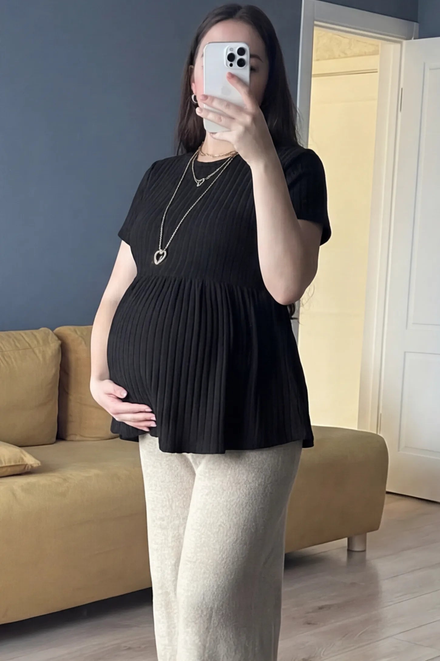 Ribbed Round Neck Short Sleeve Maternity Top in Black featuring a soft knit stretch and short sleeves on a pregnant model taking a mirror selfie indoors, front view.