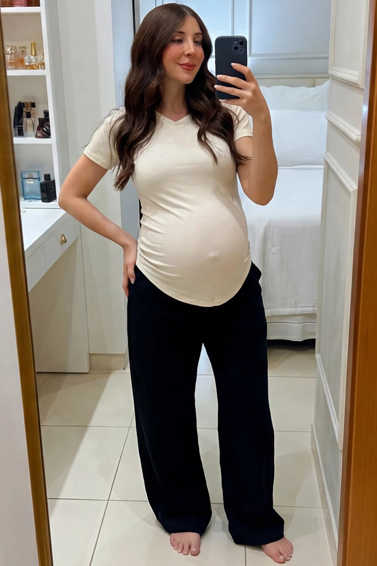 Side Ruched V-Neck Short Sleeve Maternity T-Shirt in White featuring breathable fabric and ruching on sides on a pregnant woman taking a mirror selfie indoors, front view.