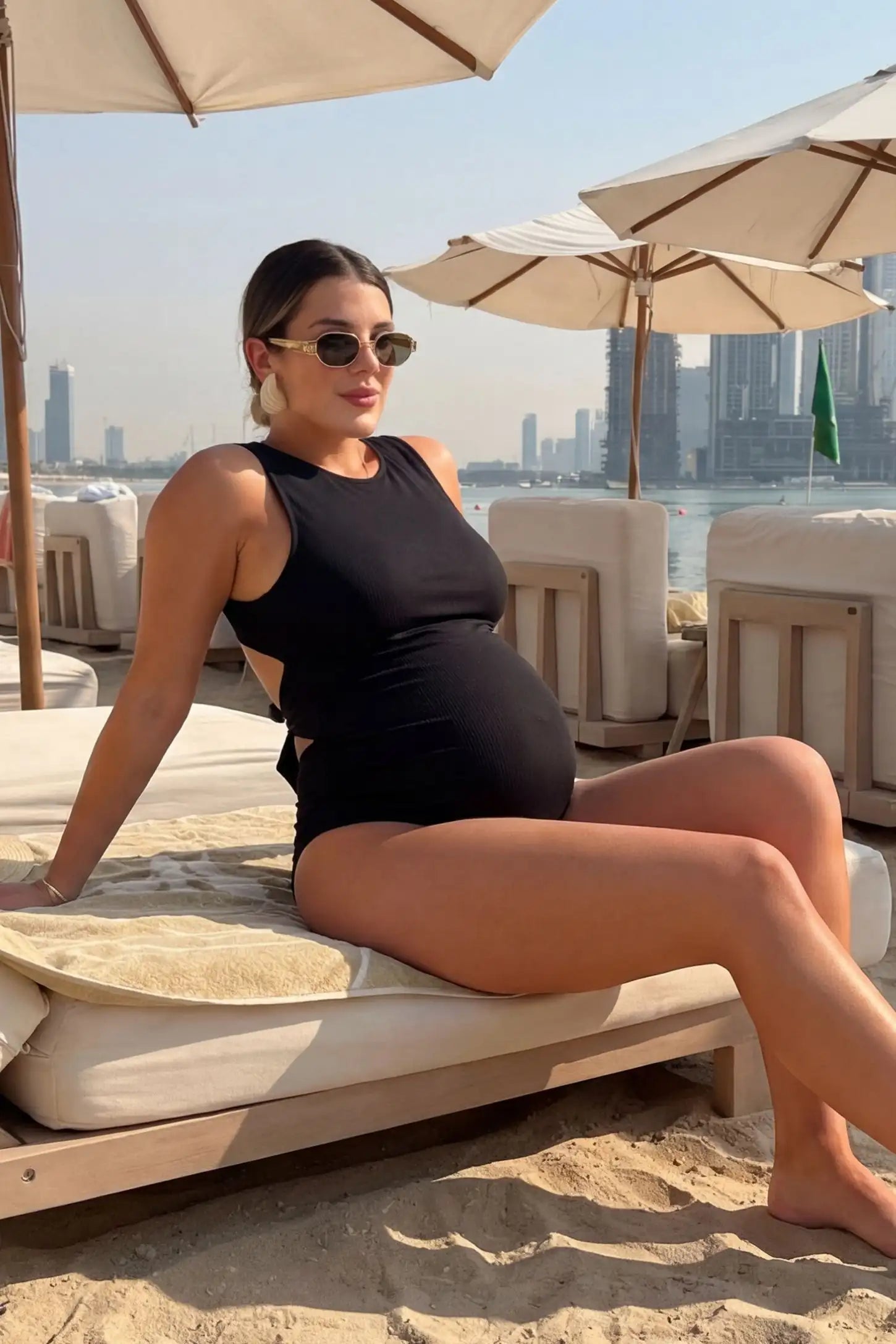 Tie-Back High-Neck Maternity Monokini in Black showing a high neck and open back on a pregnant model lounging at the beach.