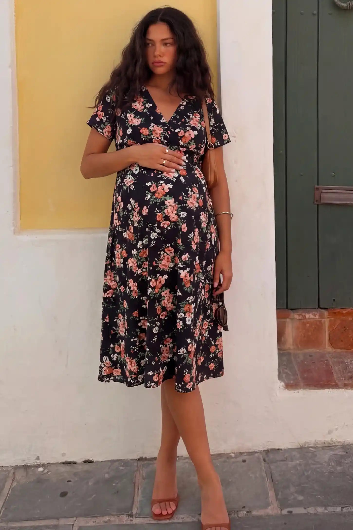 Smocked Waist Crossover Maternity Midi Dress in black floral print featuring V-neck wrap bodice and A-line midi skirt on pregnant model.