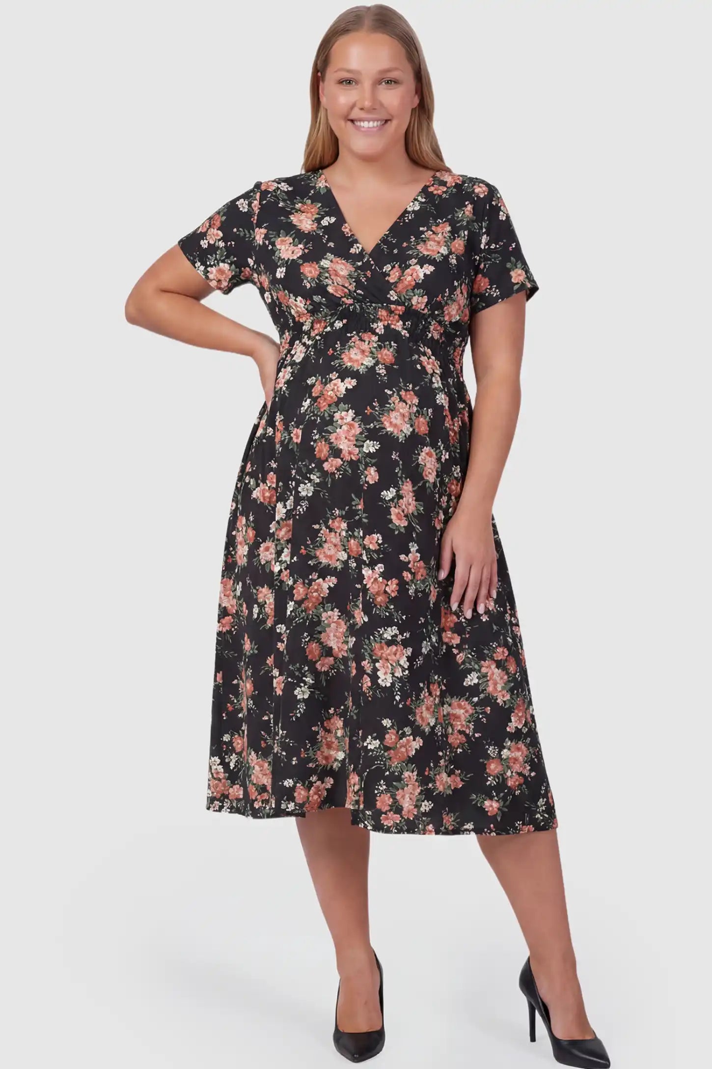 Smocked Waist Crossover Maternity Midi Dress Smocked Waist Crossover Maternity Midi Dress in black floral print featuring V-neck wrap bodice and A-line midi skirt on plus size pregnant model.