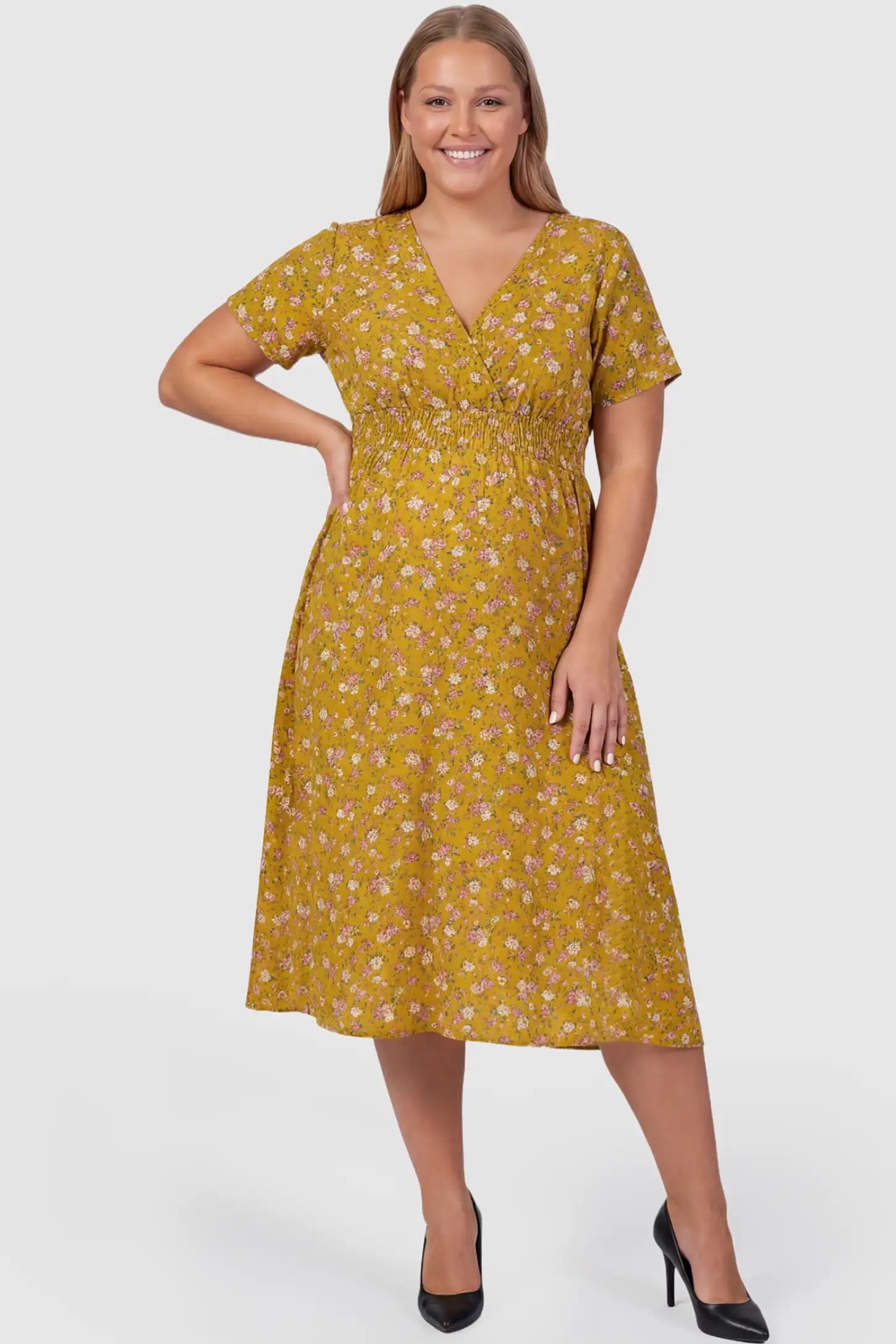 Smocked Waist Crossover Maternity Midi Dress Smocked Waist Crossover Maternity Midi Dress in yellow floral print featuring V-neck wrap bodice and A-line midi skirt on plus size pregnant model.