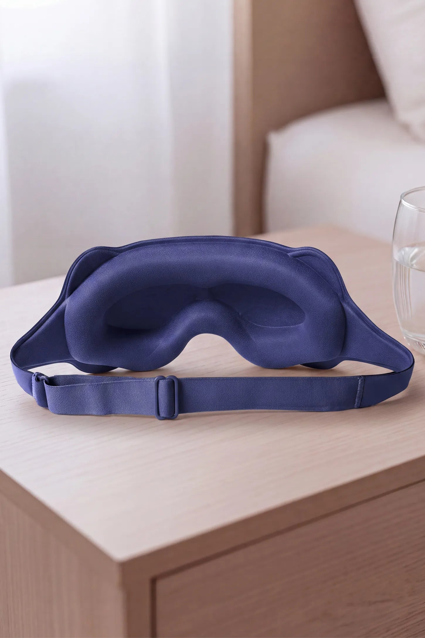 3D Contoured Blackout Sleep Mask 3D Contoured Blackout Sleep Mask in Slate Purple featuring inner eye cavity contouring, soft cushioned nose bridge, and adjustable elastic strap displayed on a wooden nightstand, lifestyle setting.