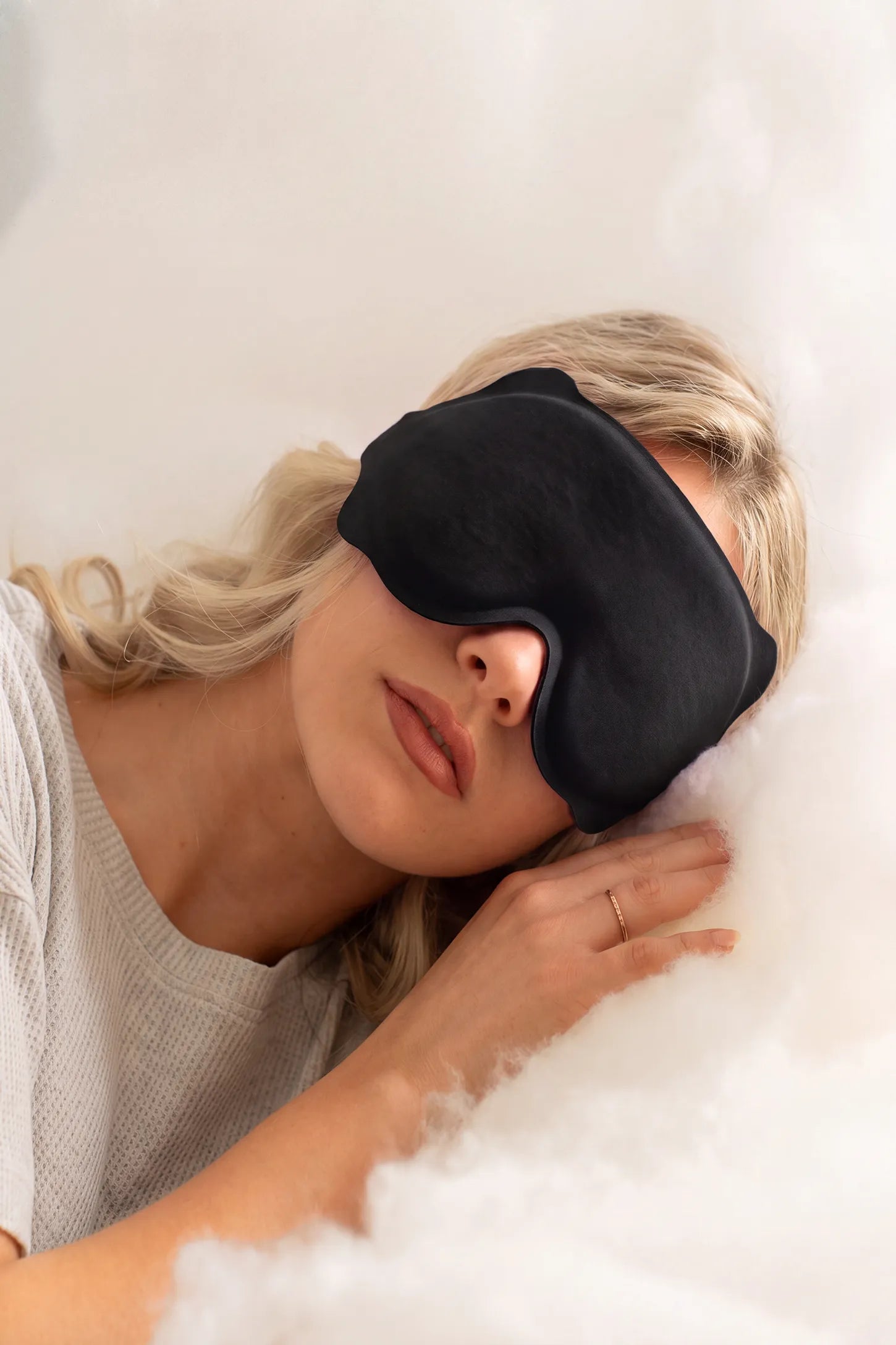 3D Contoured Blackout Sleep Mask 3D Contoured Blackout Sleep Mask in Black featuring 3D ergonomic contoured design, soft lightweight breathable fabric, total light blocking performance, and an adjustable strap worn by a woman resting in bed, lifestyle view.