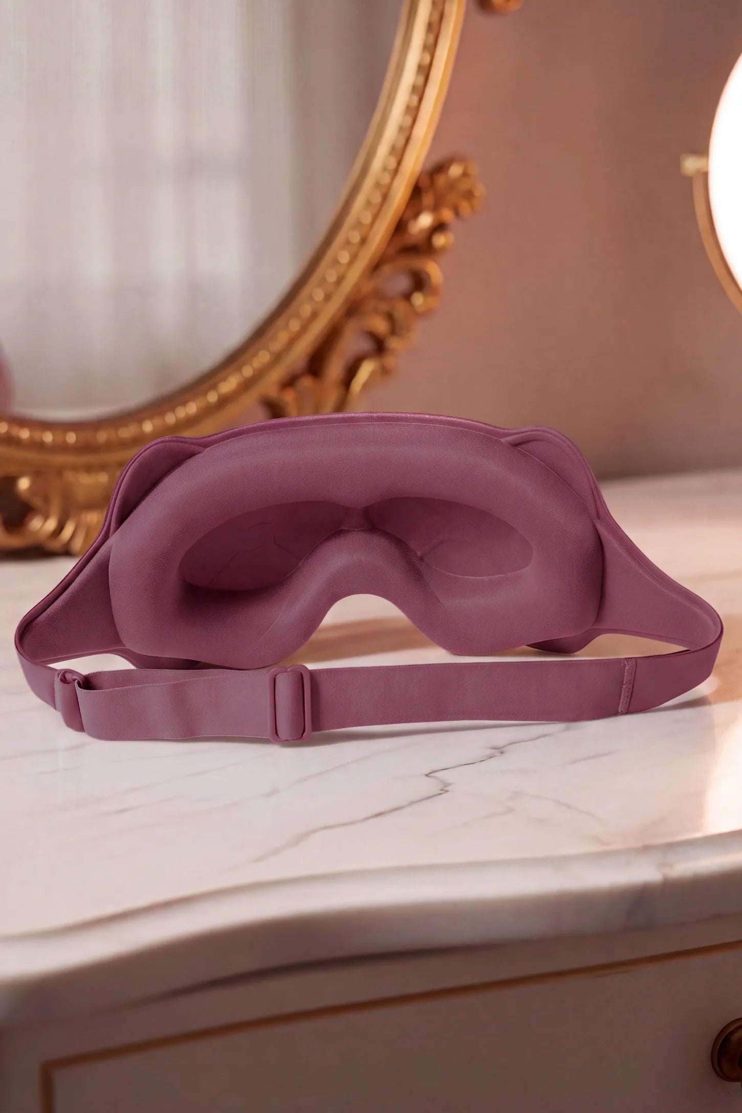 3D Contoured Blackout Sleep Mask 3D Contoured Blackout Sleep Mask in Soft Pink featuring inner eye cavity contouring, soft cushioned nose bridge, and adjustable elastic strap displayed on a wooden nightstand, lifestyle setting.
