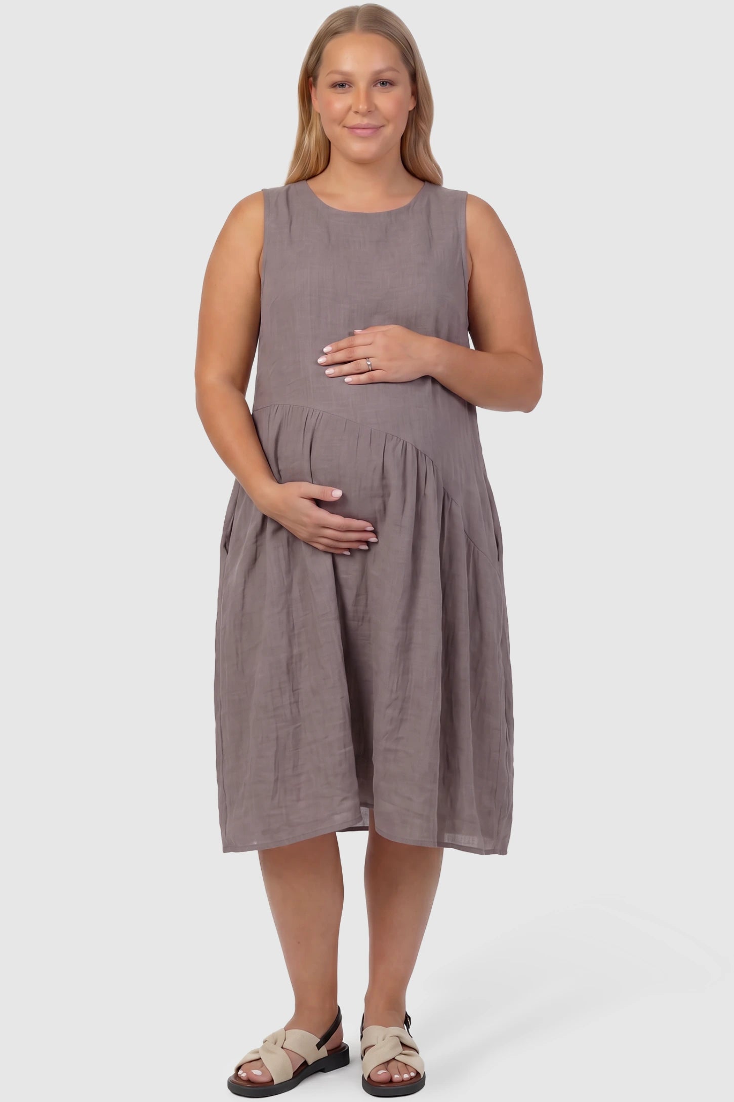Sleeveless Pocketed A-Line Maternity Midi Dress Sleeveless pocketed A-line maternity midi dress in light taupe with sleeveless cut, front view on plus-size model