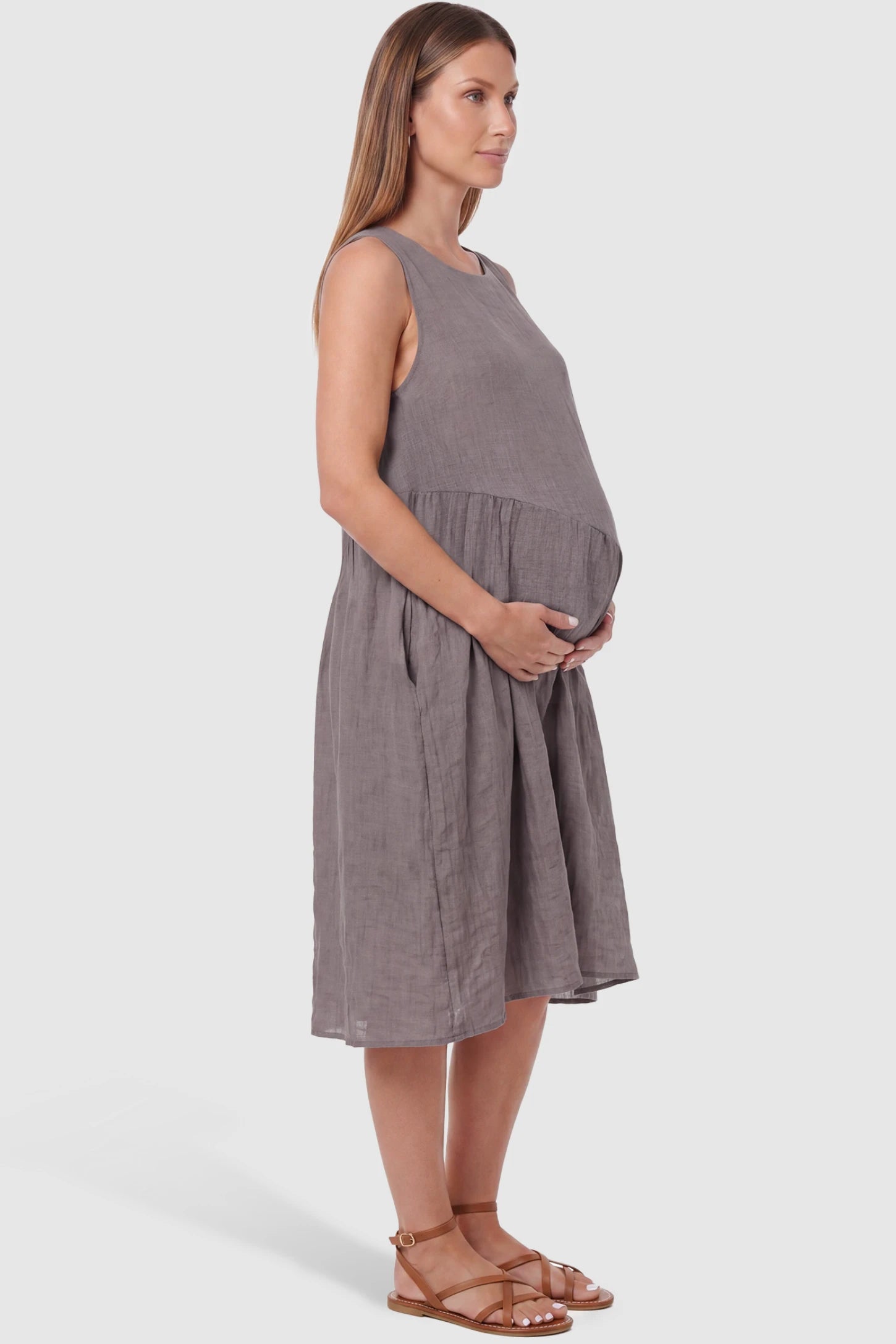 Sleeveless Pocketed A-Line Maternity Midi Dress Sleeveless pocketed A-line maternity midi dress in light taupe with sleeveless cut, side view on pregnant model