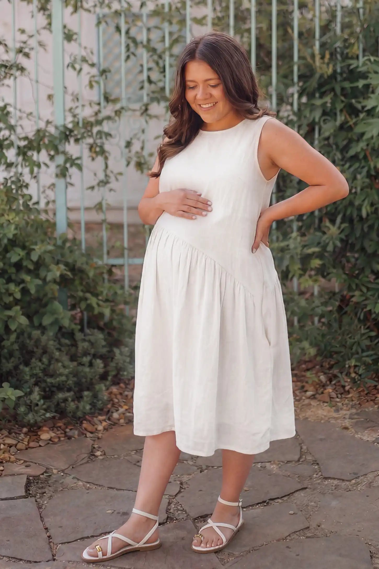 Sleeveless pocketed A-line maternity midi dress in white with sleeveless cut, front view on pregnant model