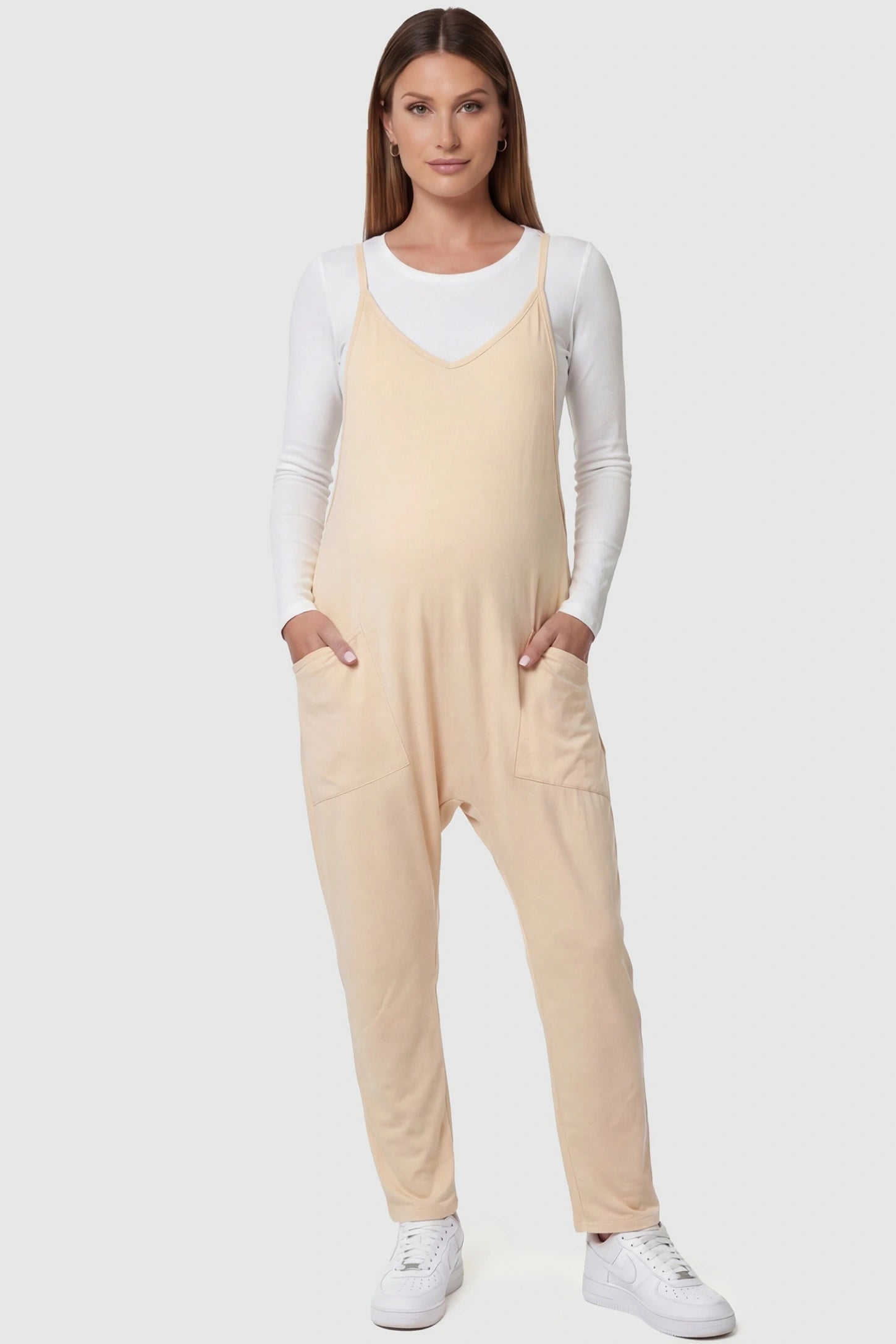 Adjustable Strap Pocketed Relaxed Maternity Jumpsuit Adjustable Strap Relaxed Maternity Jumpsuit in Beige featuring a loose fit and functional pockets on a pregnant model.