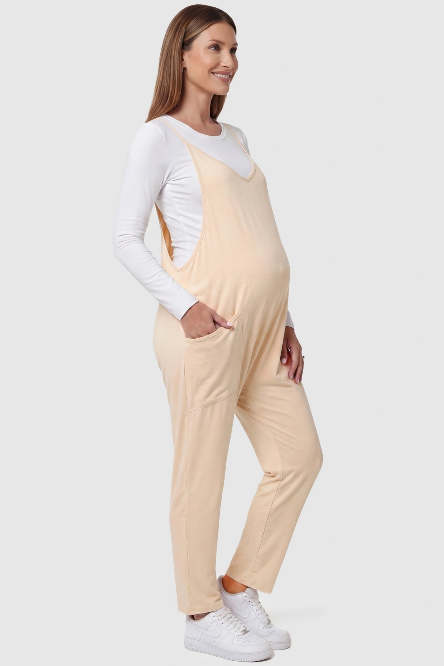 Adjustable Strap Pocketed Relaxed Maternity Jumpsuit Adjustable Strap Relaxed Maternity Jumpsuit in Beige featuring a loose fit and functional pockets on a pregnant model.