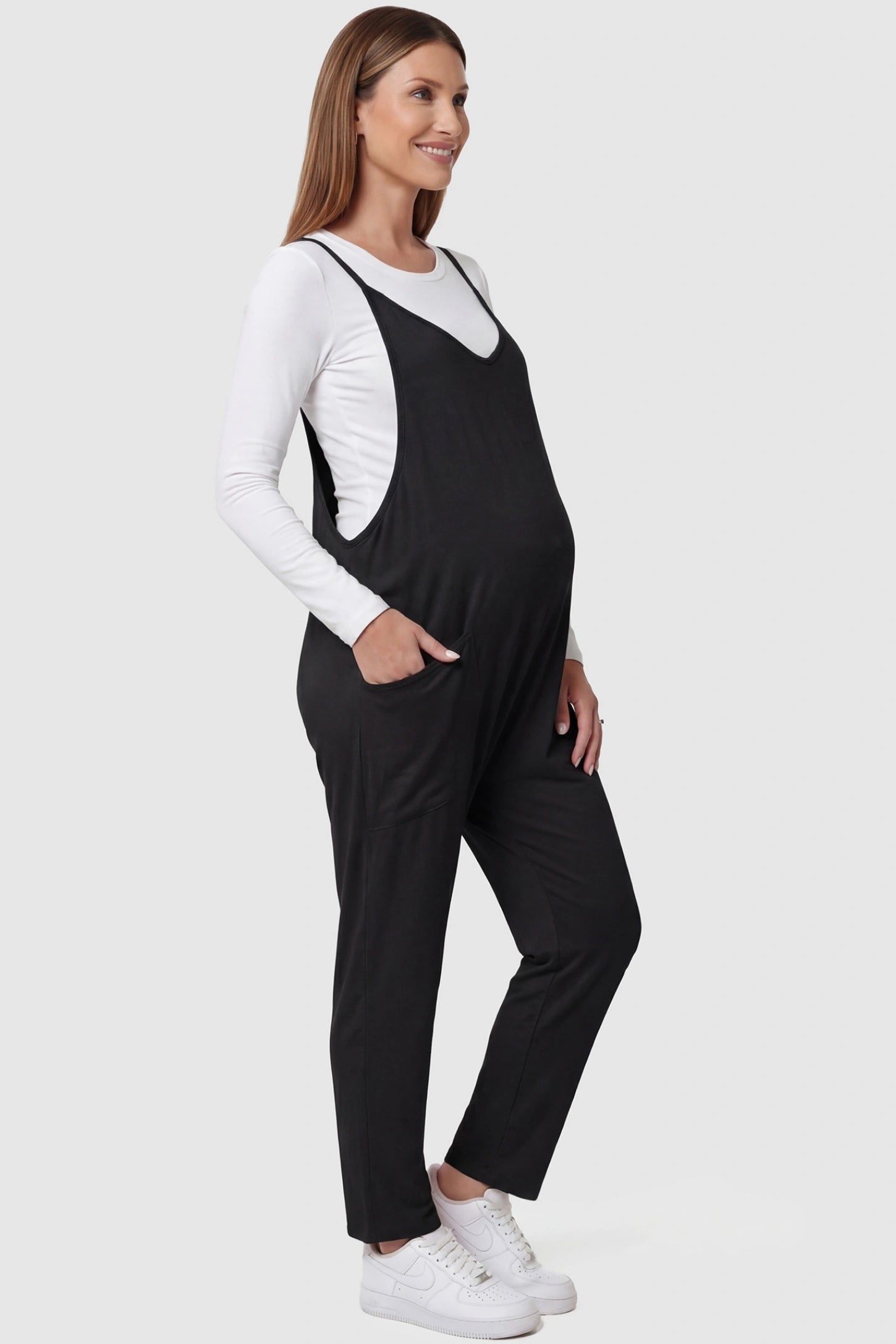 Adjustable Strap Pocketed Relaxed Maternity Jumpsuit Adjustable Strap Relaxed Maternity Jumpsuit in Black featuring a loose fit and functional pockets on a pregnant model.