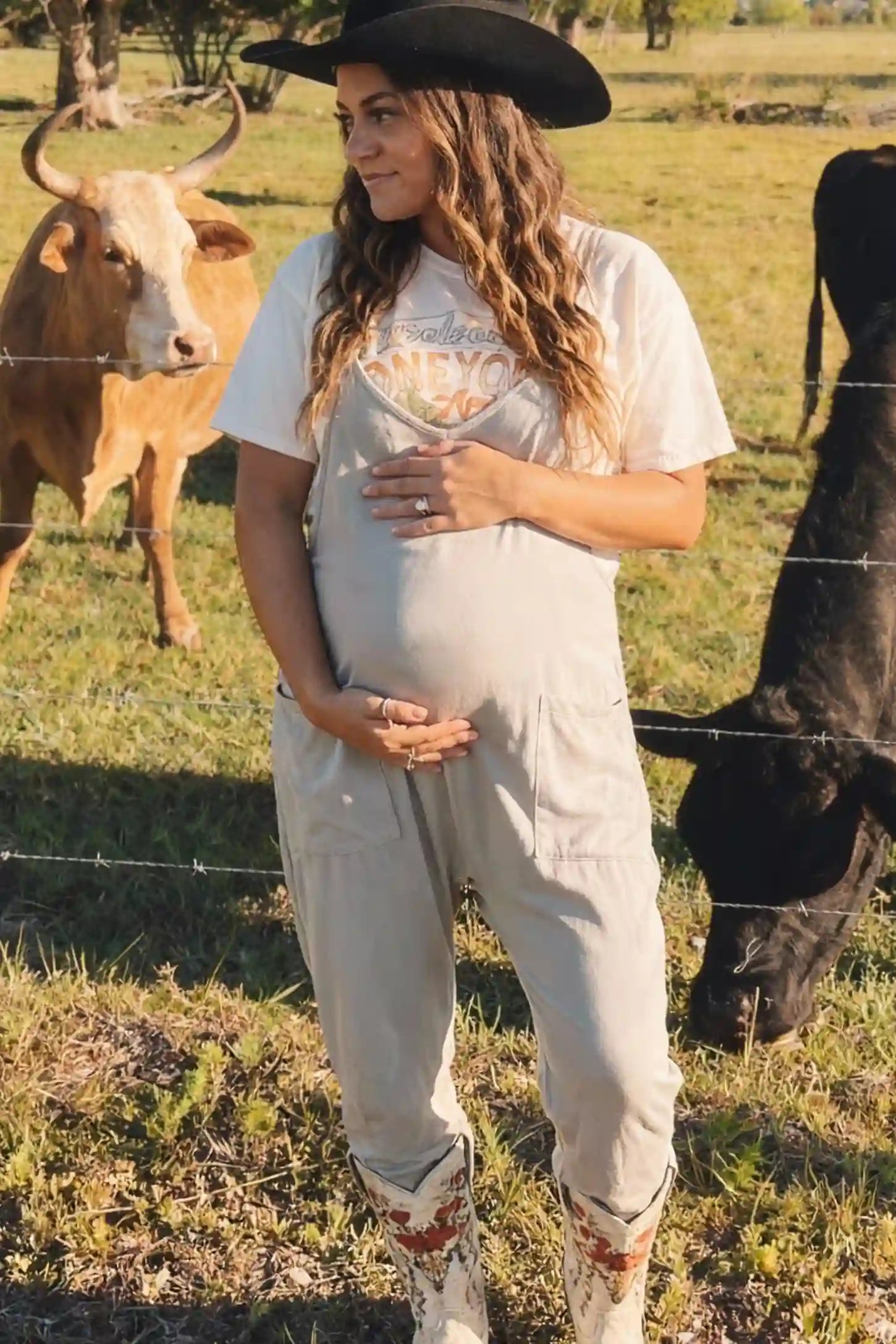 Adjustable Strap Pocketed Relaxed Maternity Jumpsuit Adjustable Strap Relaxed Maternity Jumpsuit in Light Gray featuring a loose fit and functional pockets on a pregnant model.