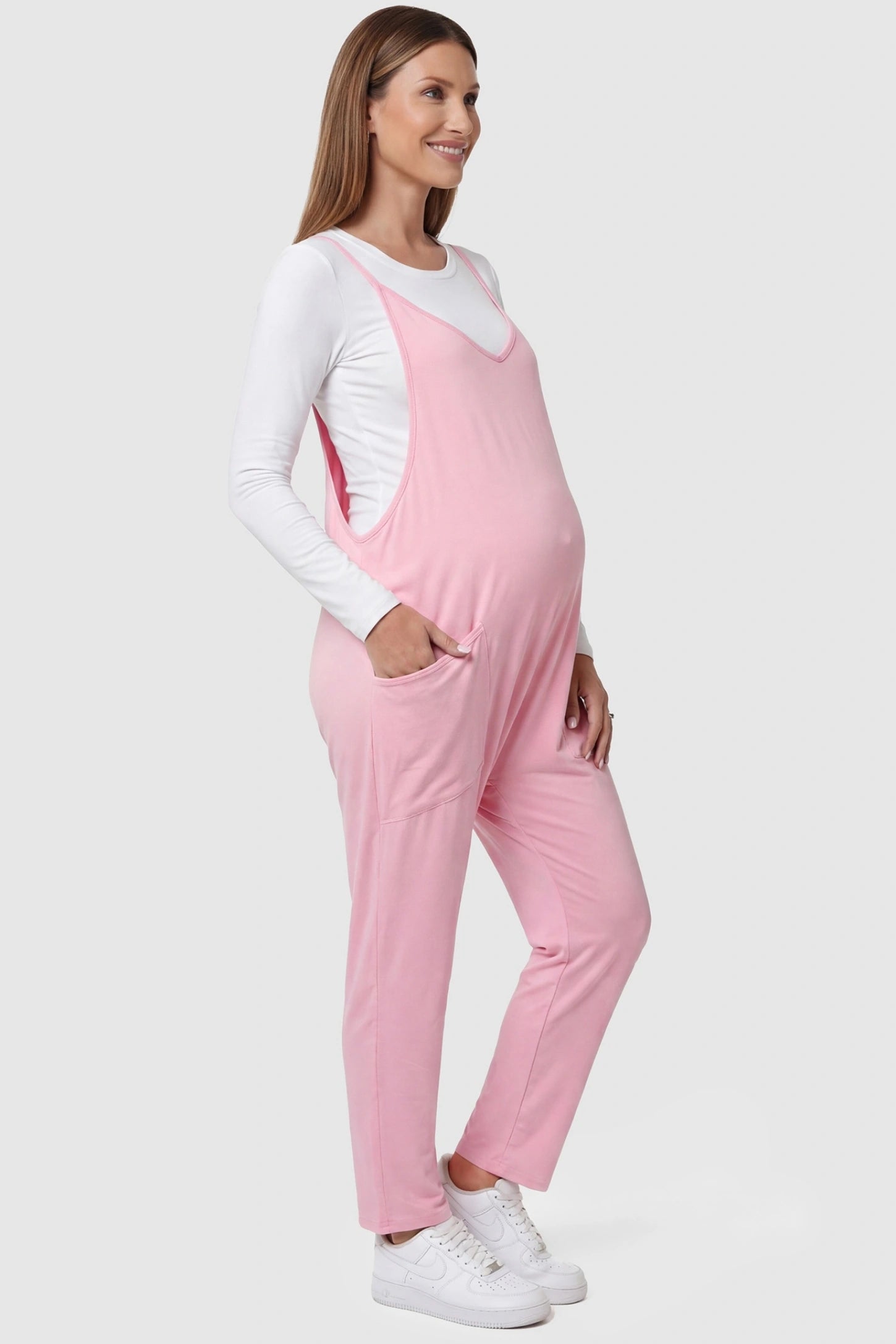 Adjustable Strap Pocketed Relaxed Maternity Jumpsuit Adjustable Strap Relaxed Maternity Jumpsuit in Pink featuring a loose fit and functional pockets on a pregnant model.