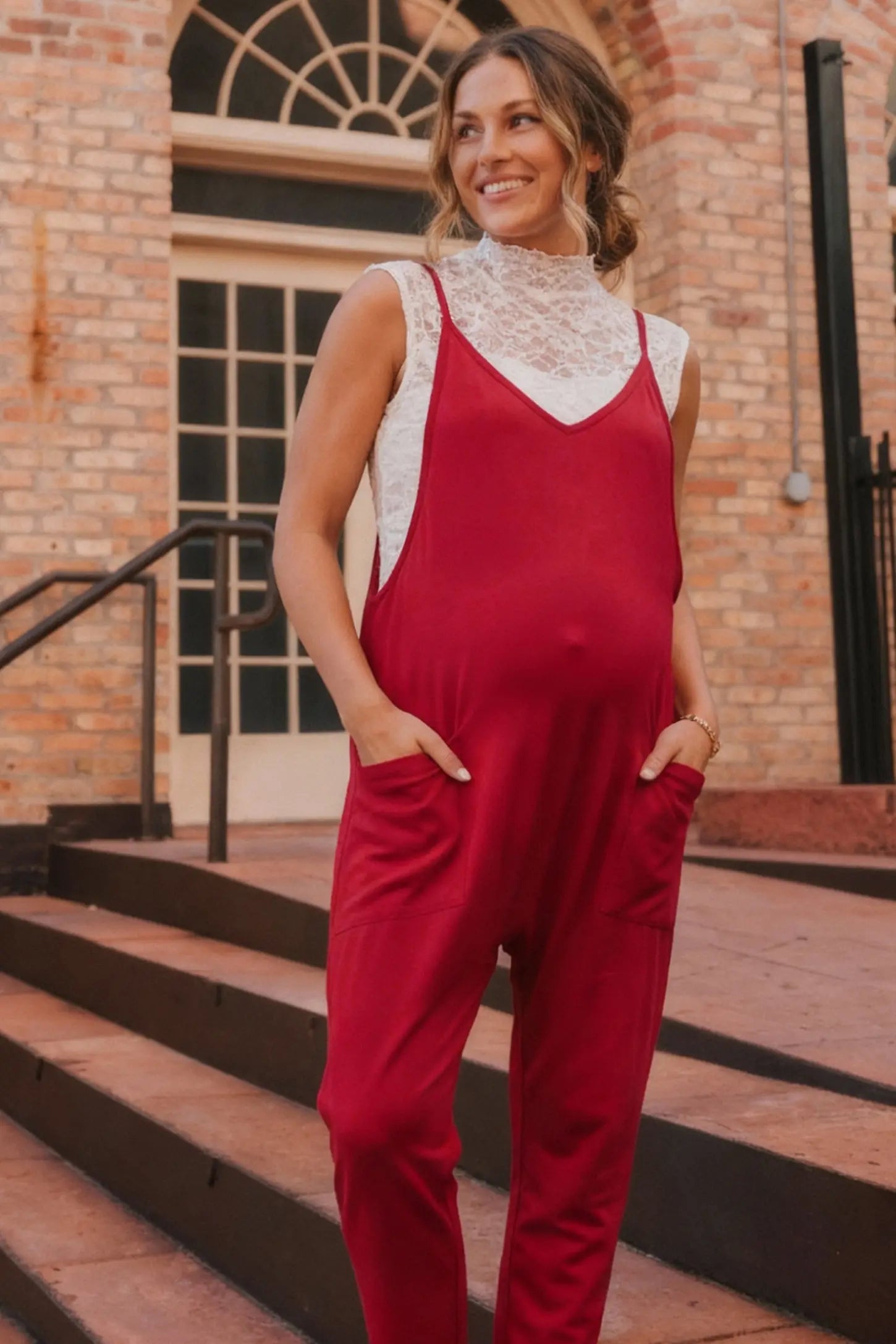 Adjustable Strap Pocketed Relaxed Maternity Jumpsuit Adjustable Strap Relaxed Maternity Jumpsuit in Wine Red featuring a loose fit and functional pockets on a pregnant model.