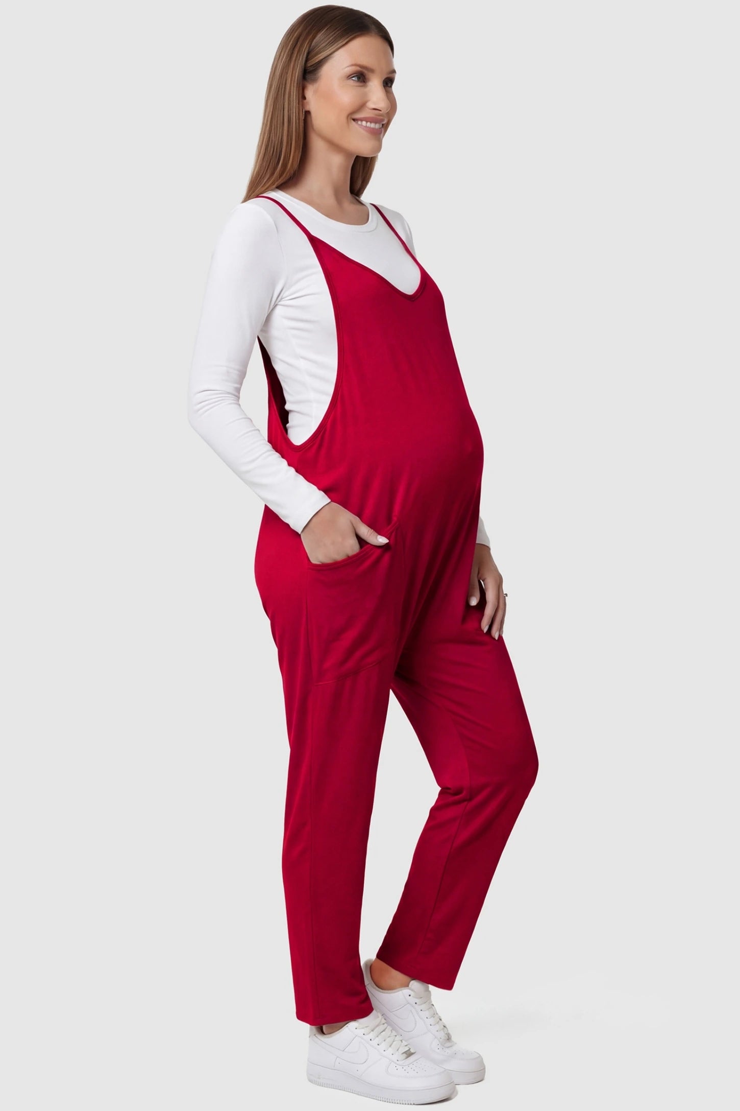 Adjustable Strap Pocketed Relaxed Maternity Jumpsuit Adjustable Strap Relaxed Maternity Jumpsuit in Wine Red featuring a loose fit and functional pockets on a pregnant model.