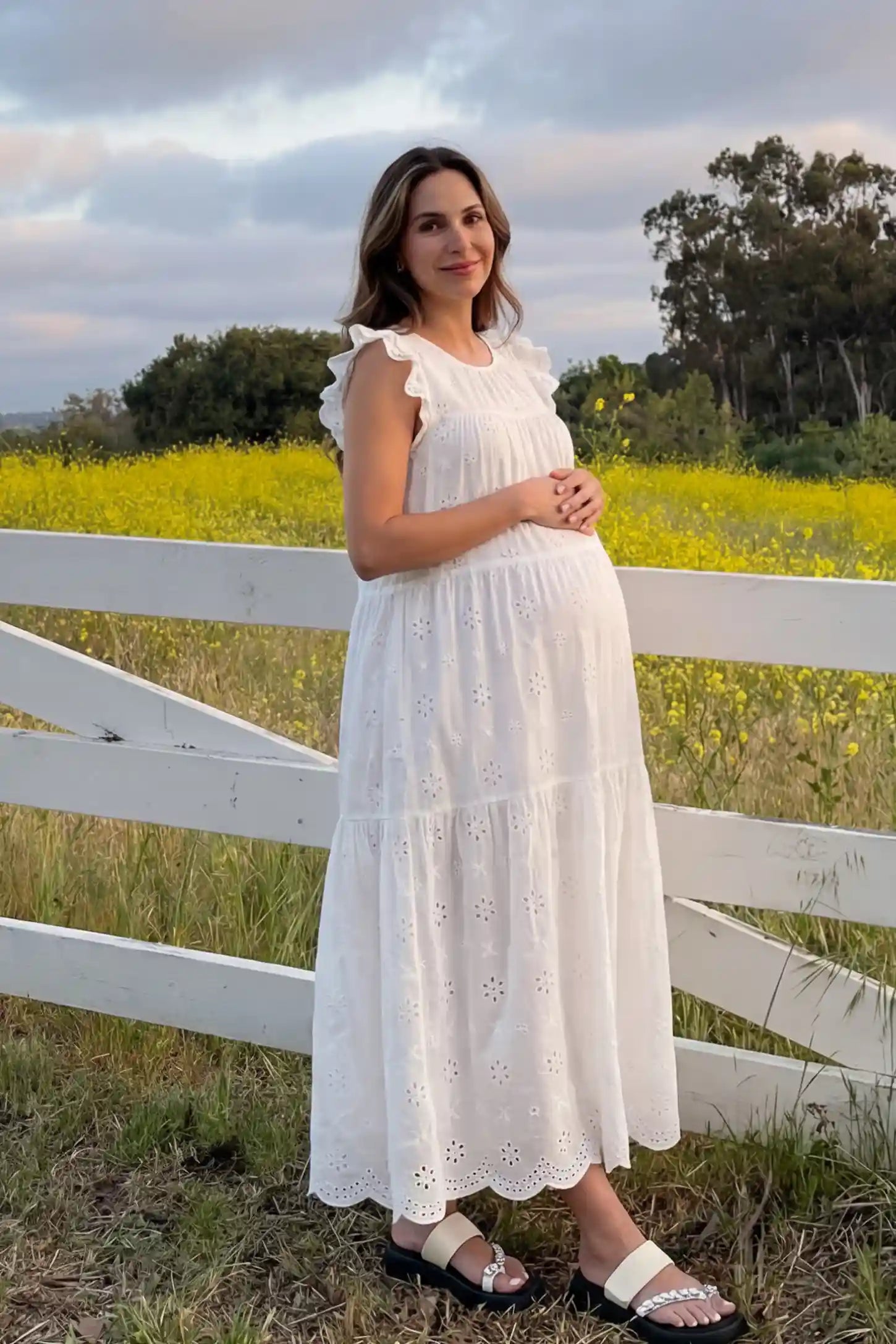Anglaise lace ruffled sleeve tiered maternity maxi dress in white with delicate lace detail, side view on pregnant model