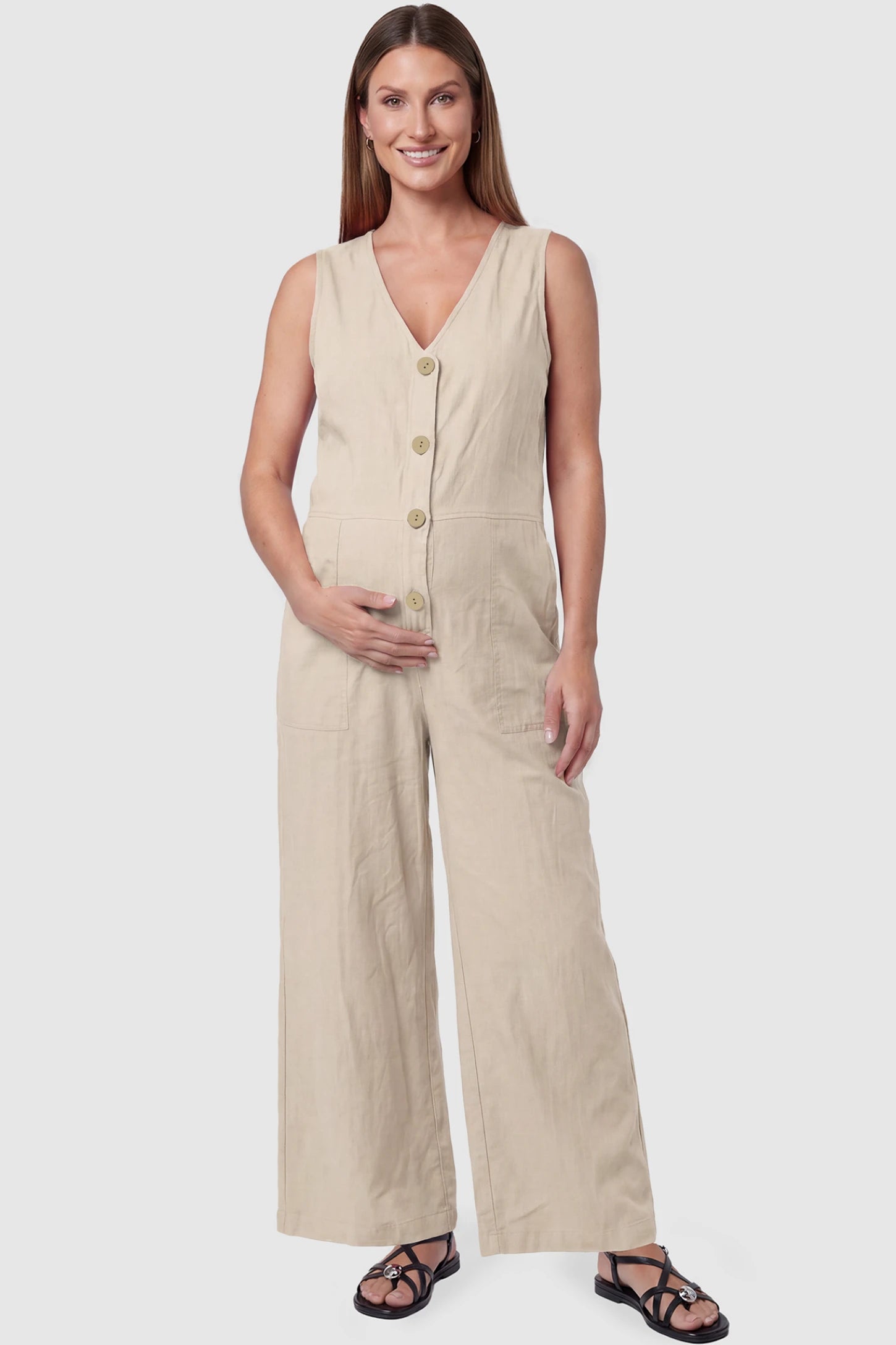 Wide-Leg V-Neck Button-Front Maternity Jumpsuit Wide-leg V-neck button-front maternity jumpsuit in beige with sleeveless V-neckline and button-front detail, front view on pregnant model