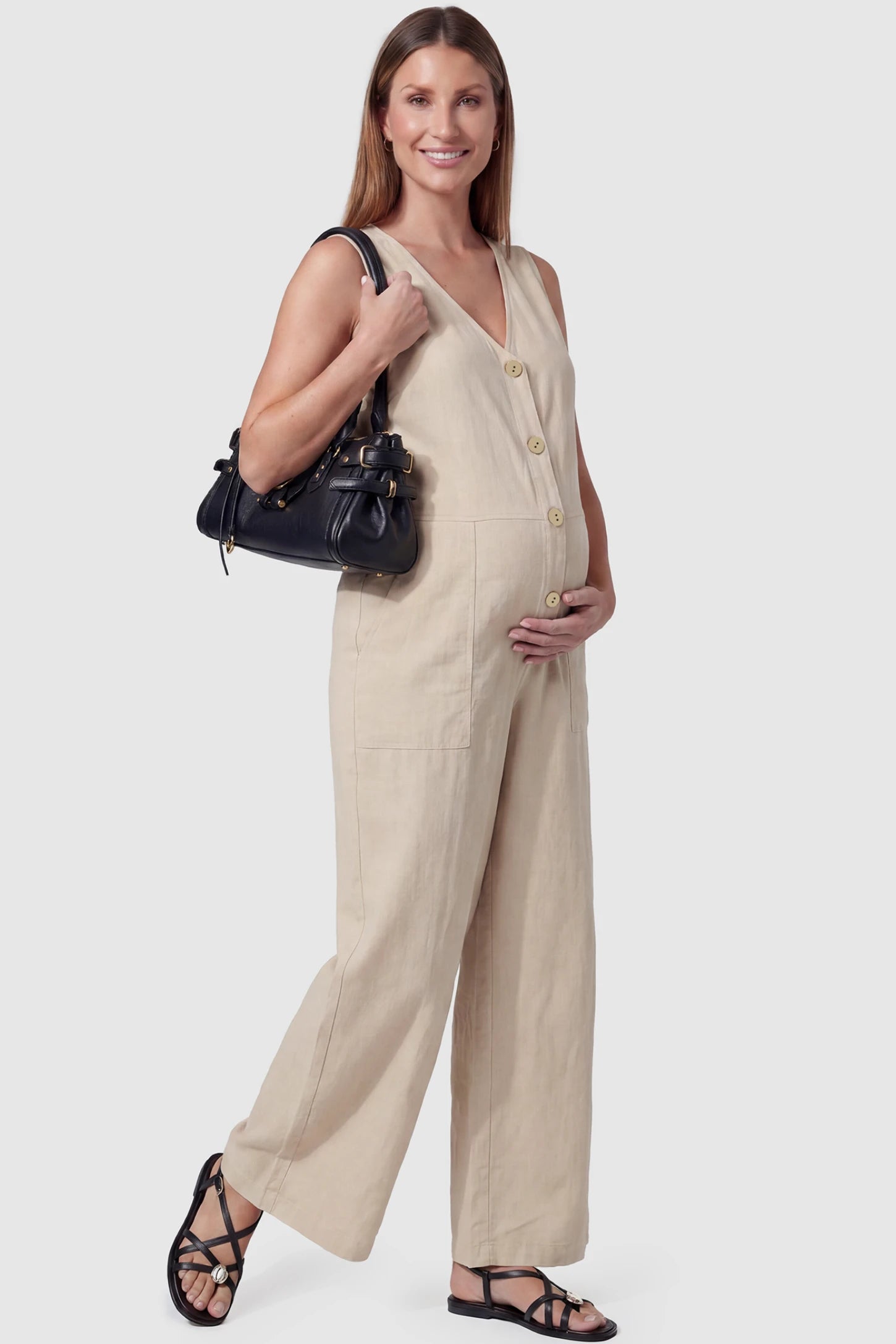 Wide-Leg V-Neck Button-Front Maternity Jumpsuit Wide-leg V-neck button-front maternity jumpsuit in beige with sleeveless V-neckline and button-front detail, side view on pregnant model