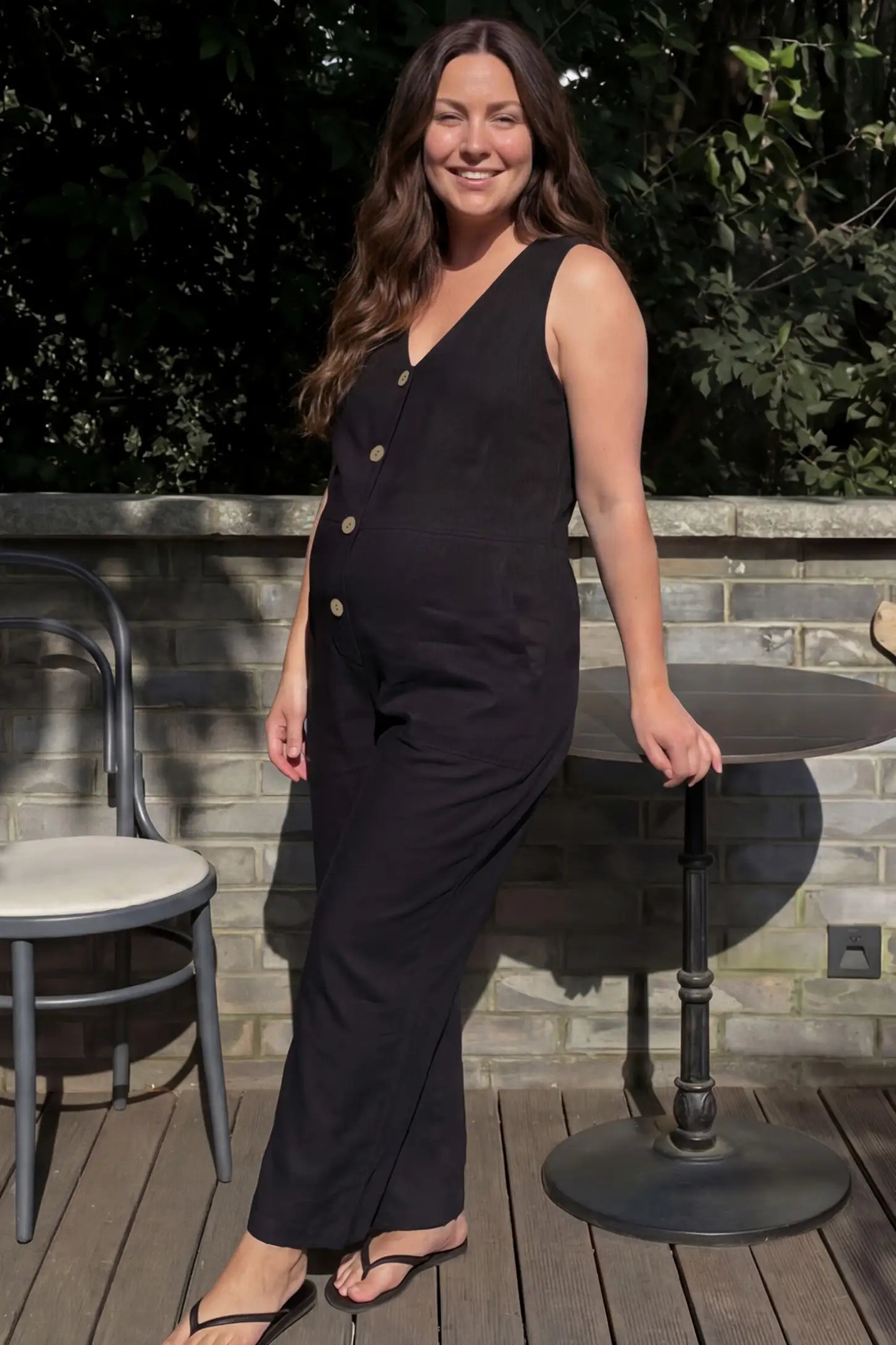 Wide-Leg V-Neck Button-Front Maternity Jumpsuit Wide-leg V-neck button-front maternity jumpsuit in black with sleeveless V-neckline and button-front detail, front view on pregnant model