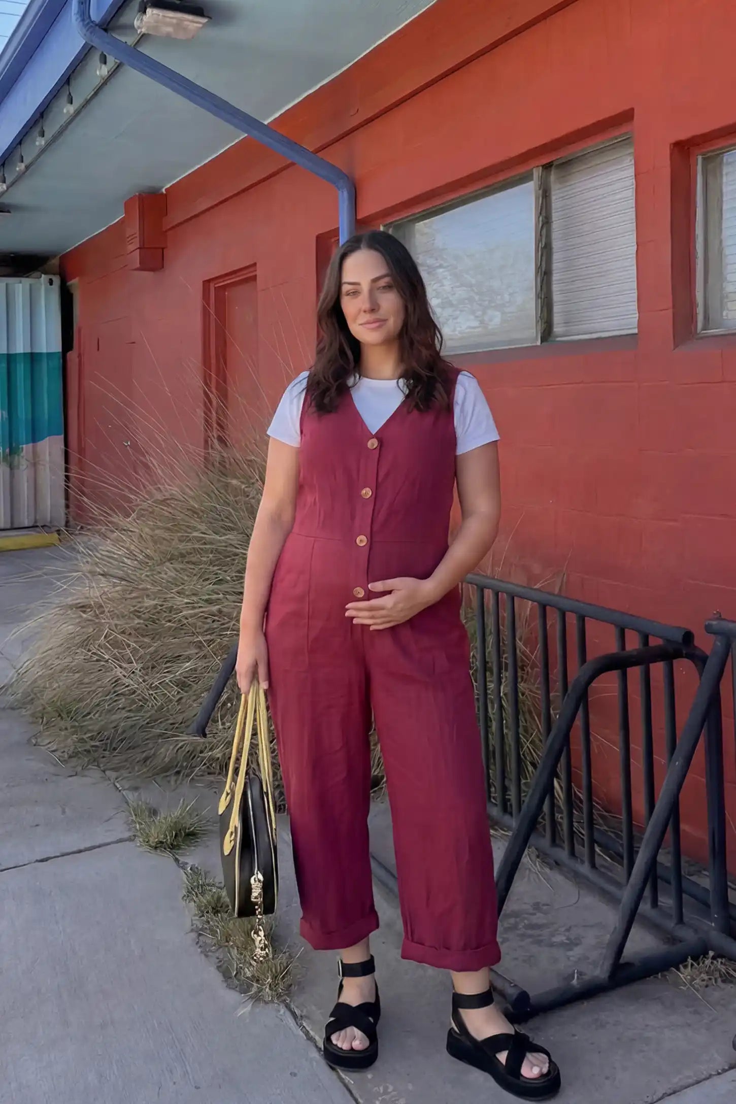 Wide-Leg V-Neck Button-Front Maternity Jumpsuit Wide-leg V-neck button-front maternity jumpsuit in wine red with sleeveless V-neckline and button-front detail, front view on pregnant model