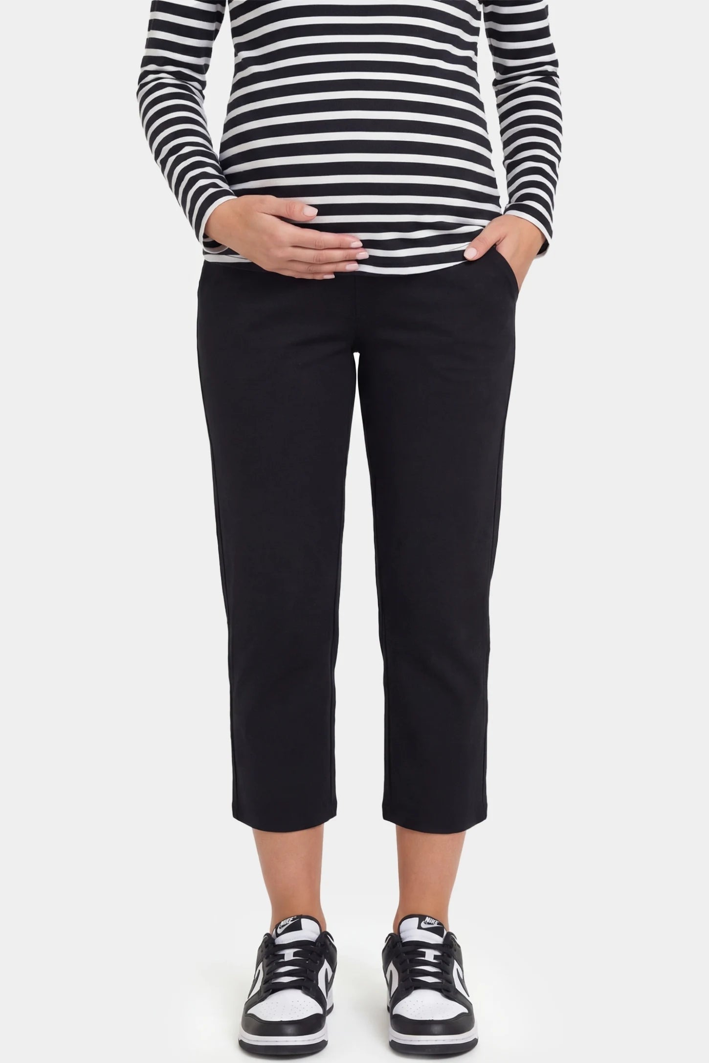 High-waist belly support loose-fit capri maternity pants in black with functional side pockets, front view on pregnant model