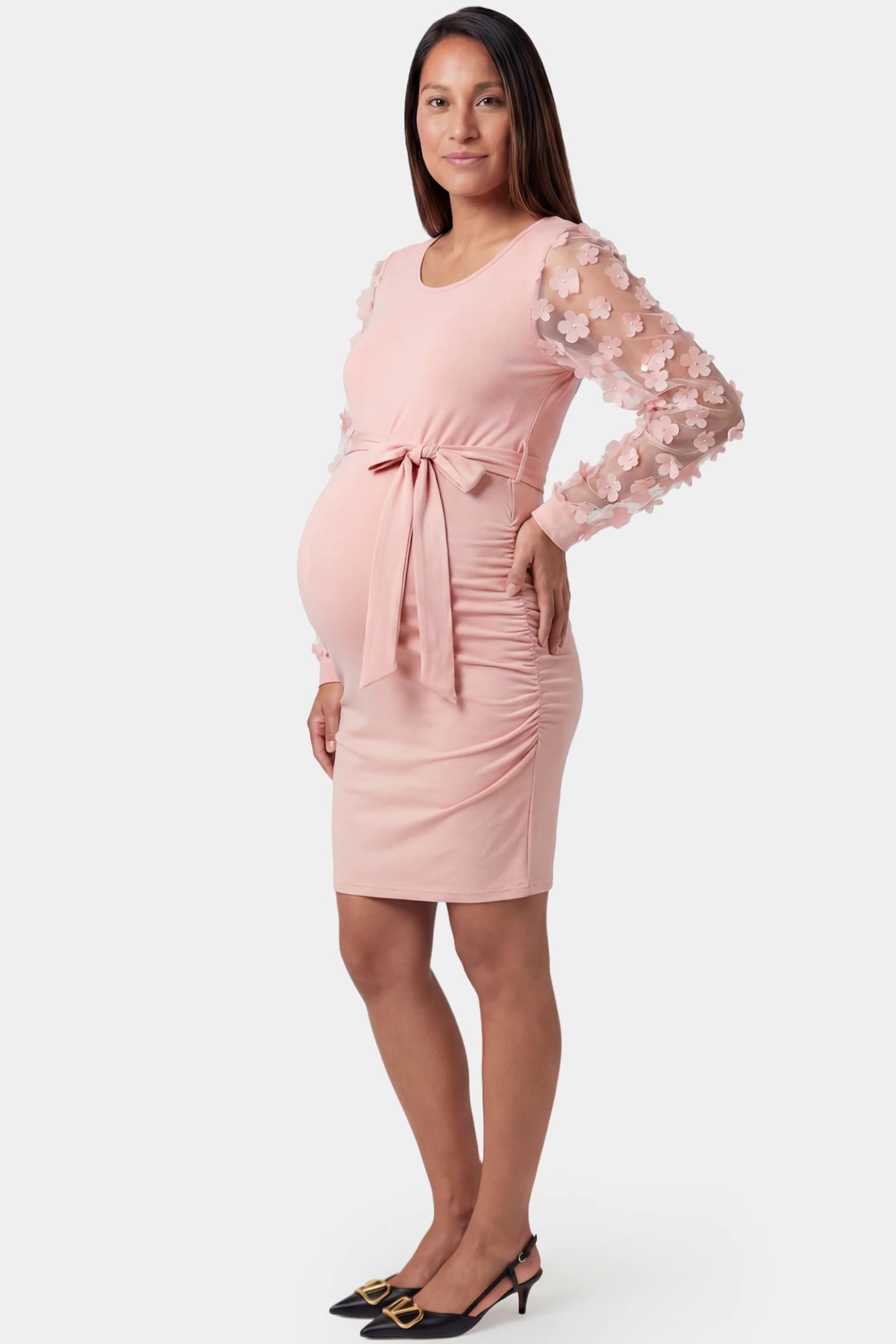 Sheer long-sleeve tie-waist short maternity dress in pink featuring side ruching detail in side view on a pregnant model