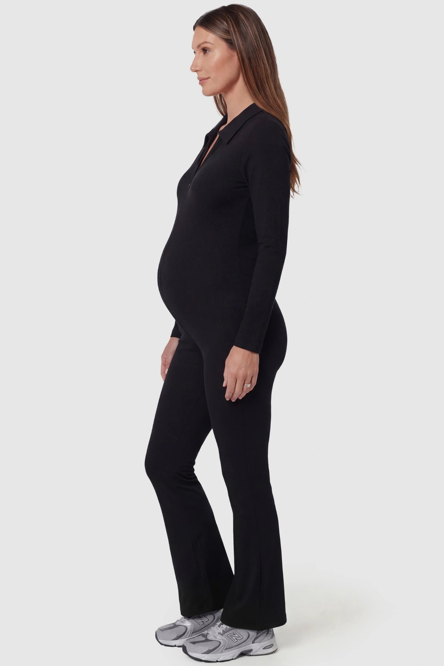 Collared Zip-Front Flared Maternity Jumpsuit Collared Zip-Front Flared Maternity Jumpsuit in Black featuring a figure shaping silhouette on a pregnant model, side view.