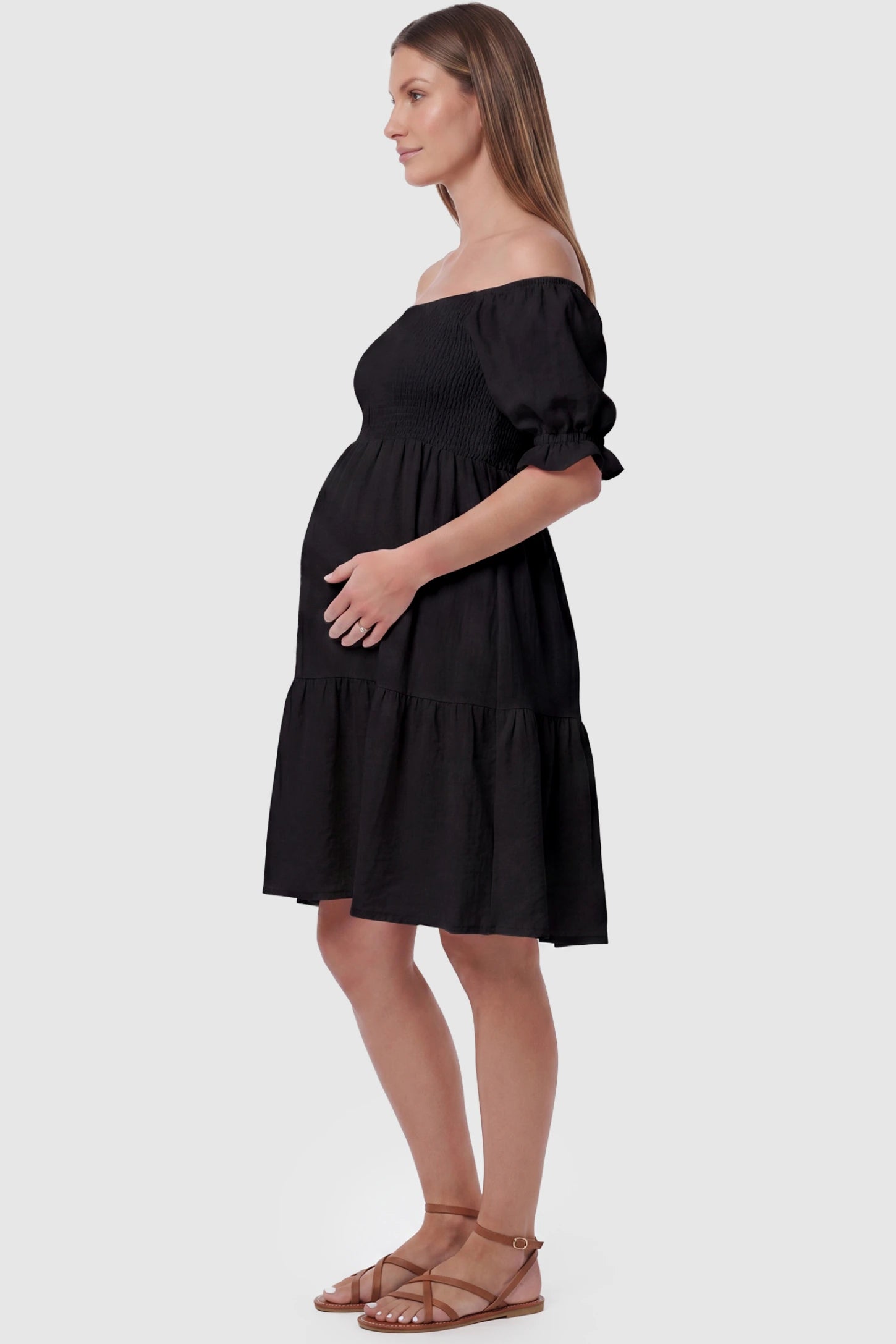 Smocked Off-Shoulder Empire Waist Maternity Short Dress Smocked off-shoulder empire waist maternity short dress in black with bump-friendly empire waist fit, side view on pregnant model