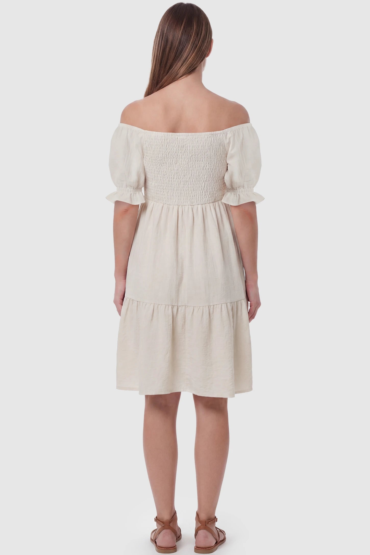 Smocked Off-Shoulder Empire Waist Maternity Short Dress Smocked off-shoulder empire waist maternity short dress in khaki with short puff sleeve, back view on pregnant model