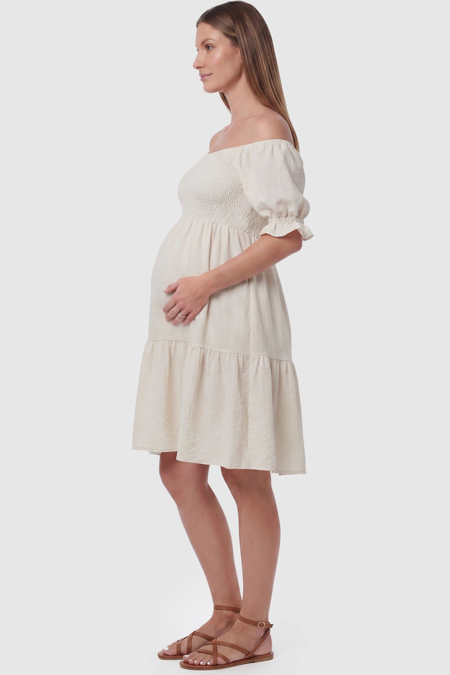 Smocked Off-Shoulder Empire Waist Maternity Short Dress Smocked off-shoulder empire waist maternity short dress in khaki with bump-friendly empire waist fit, side view on pregnant model