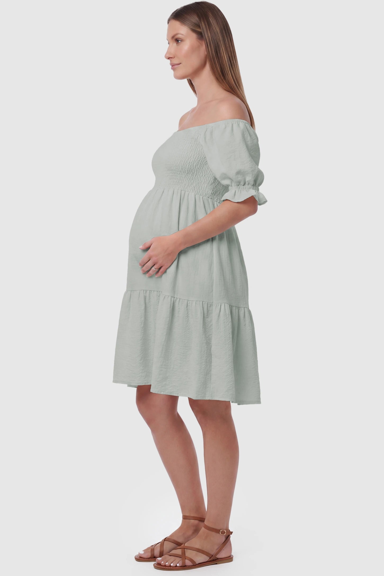 Smocked Off-Shoulder Empire Waist Maternity Short Dress Smocked off-shoulder empire waist maternity short dress in light green with bump-friendly empire waist fit, side view on pregnant model