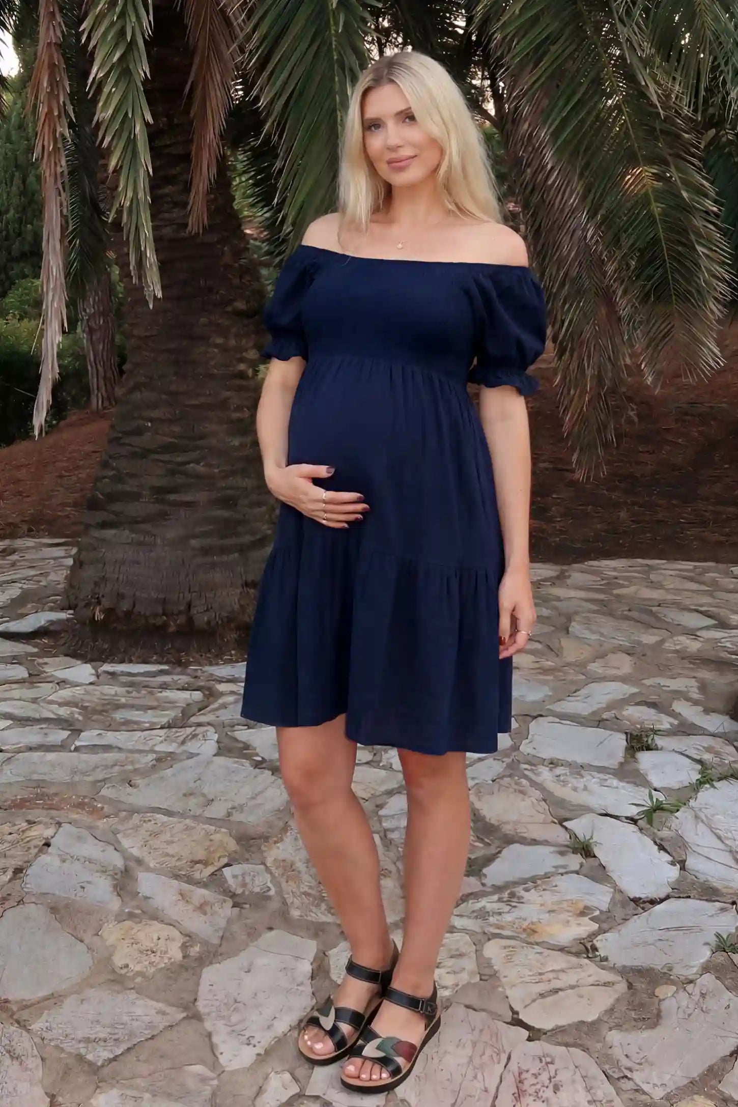 Smocked Off-Shoulder Empire Waist Maternity Short Dress Smocked off-shoulder empire waist maternity short dress in navy blue with smocked bodice detail, front view on pregnant model